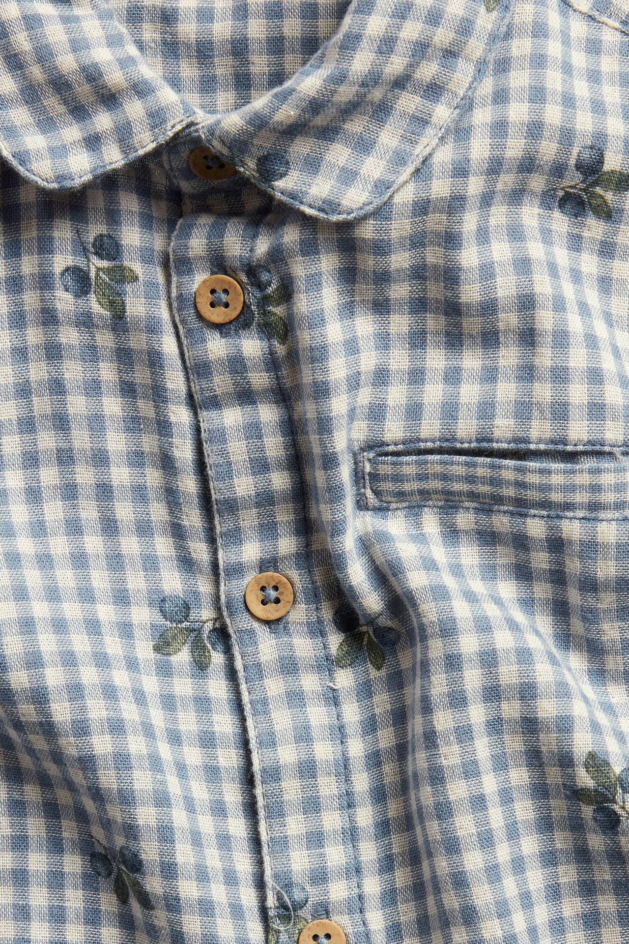 Close-up: blue-white gingham cotton shirt with blueberry print, collar, wood buttons, and pocket.