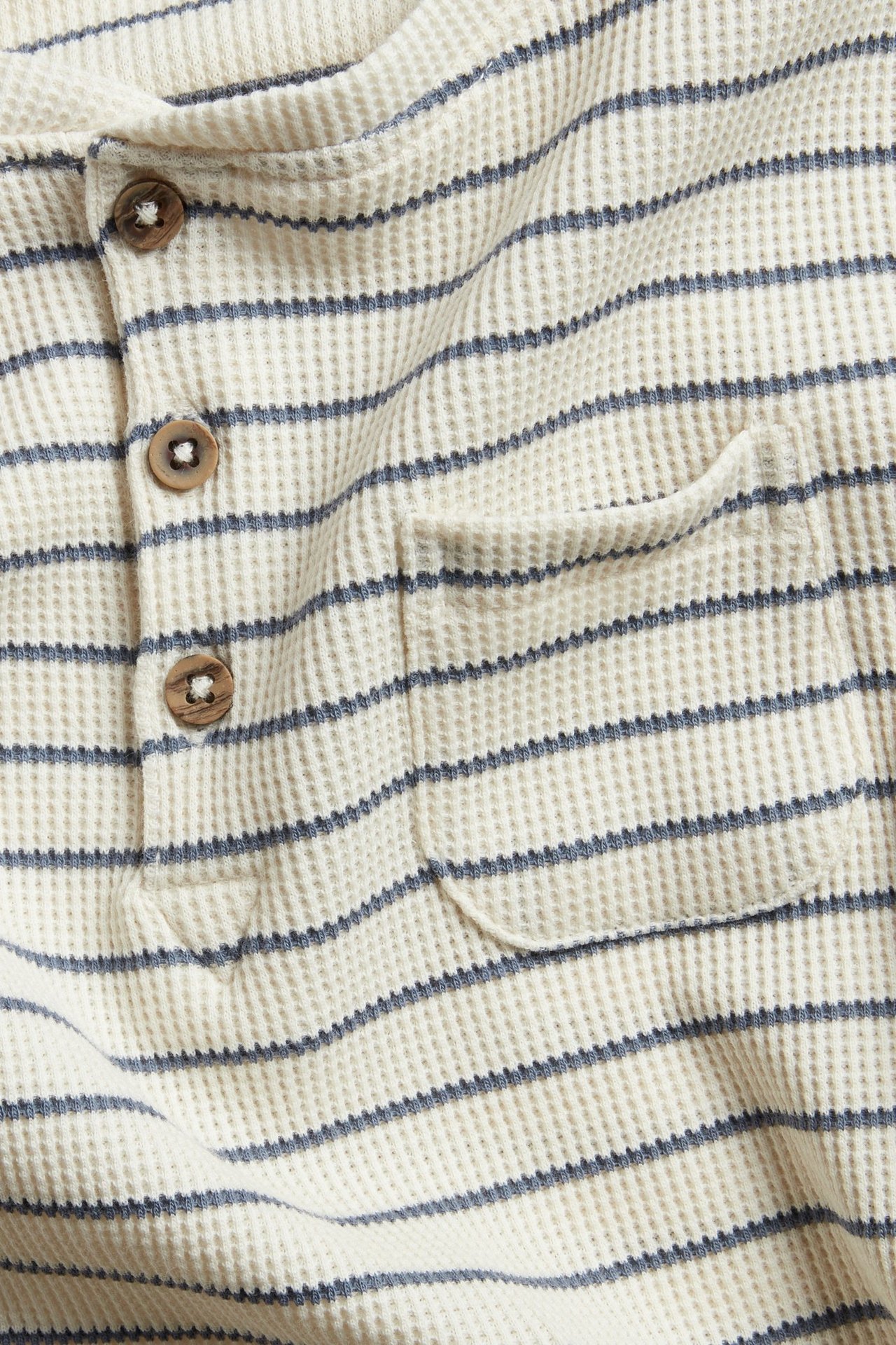 Close-up of an off-white, blue-striped waffle-knit long-sleeved top with three wooden buttons and a chest pocket.