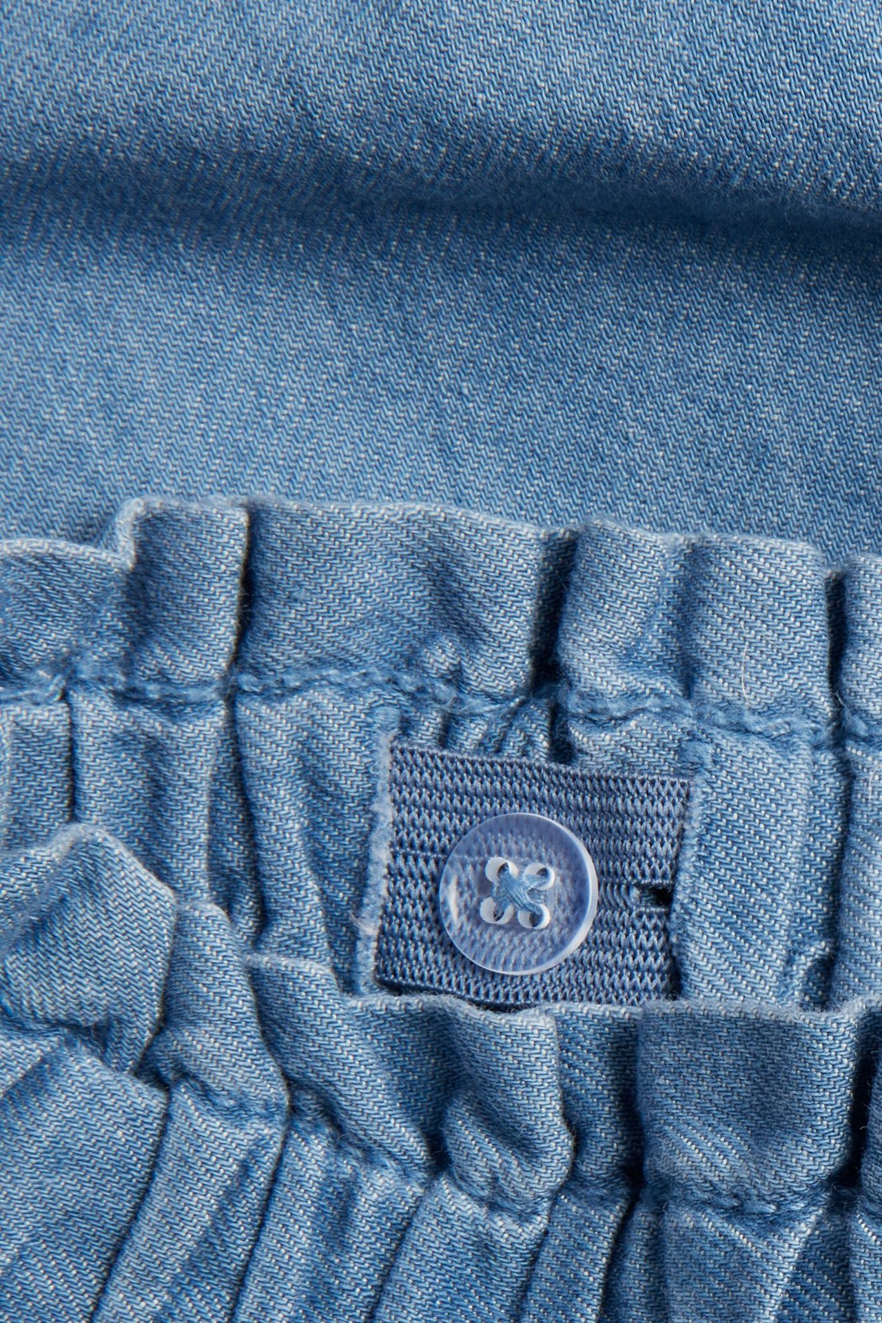 Close-up of light blue denim shorts with an adjustable elastic waistband and clear button.