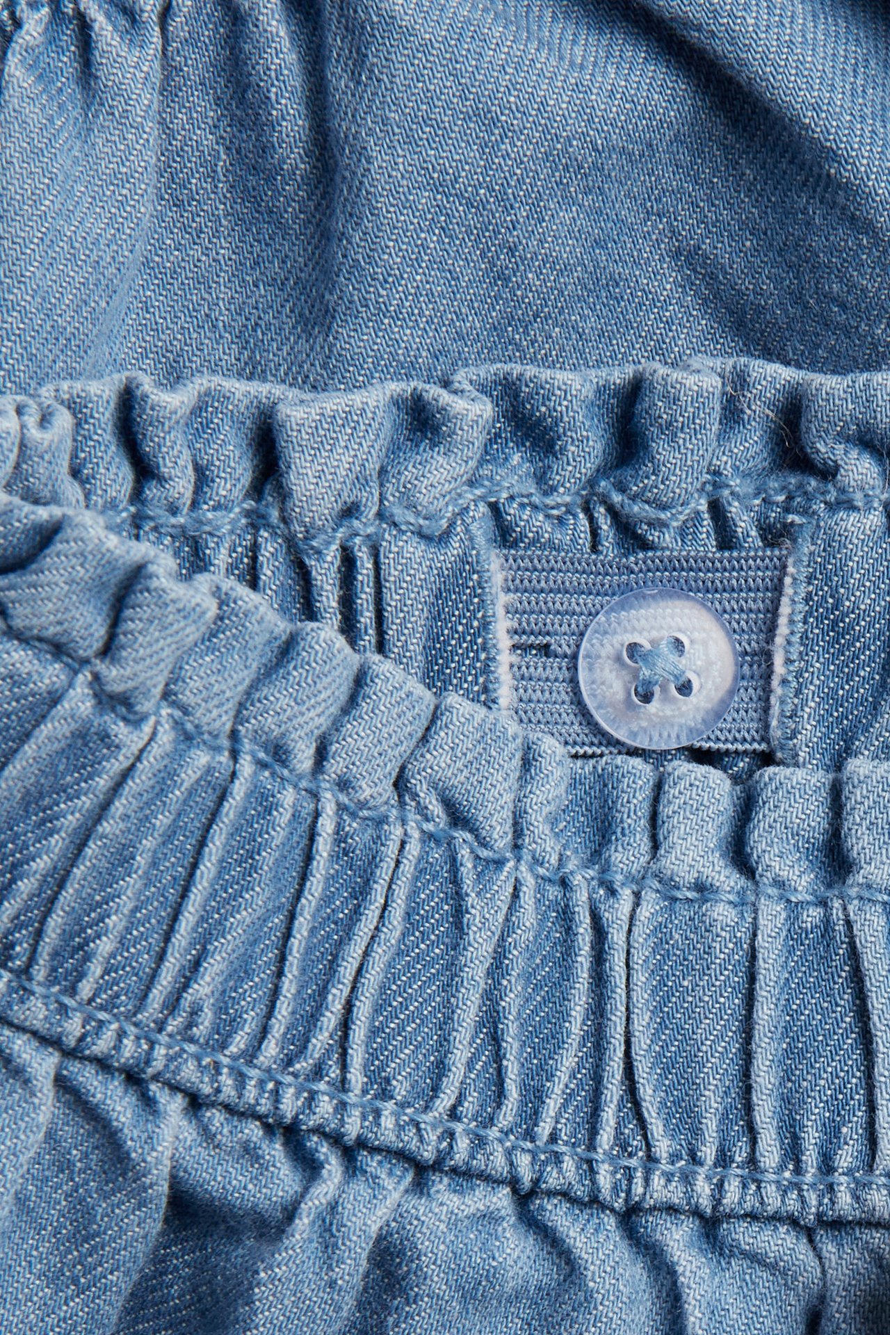 Nahaufnahme hellblauer Denim-Shorts, zeigt den elastischen Bund mit verstellbarem Knopf und Gummiband.