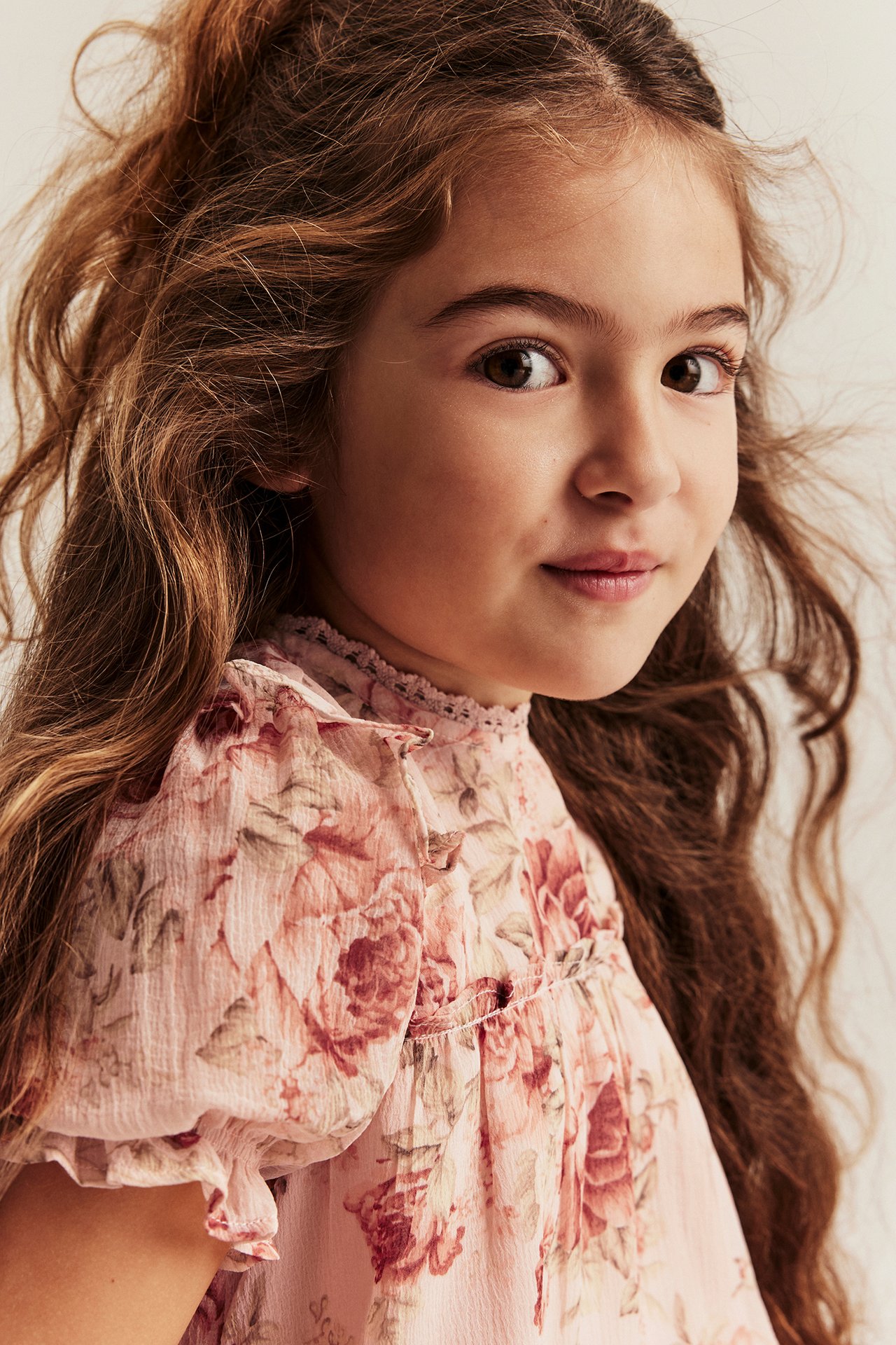 Close-up front view of a kid wearing a pink floral chiffon dress with ruffles.