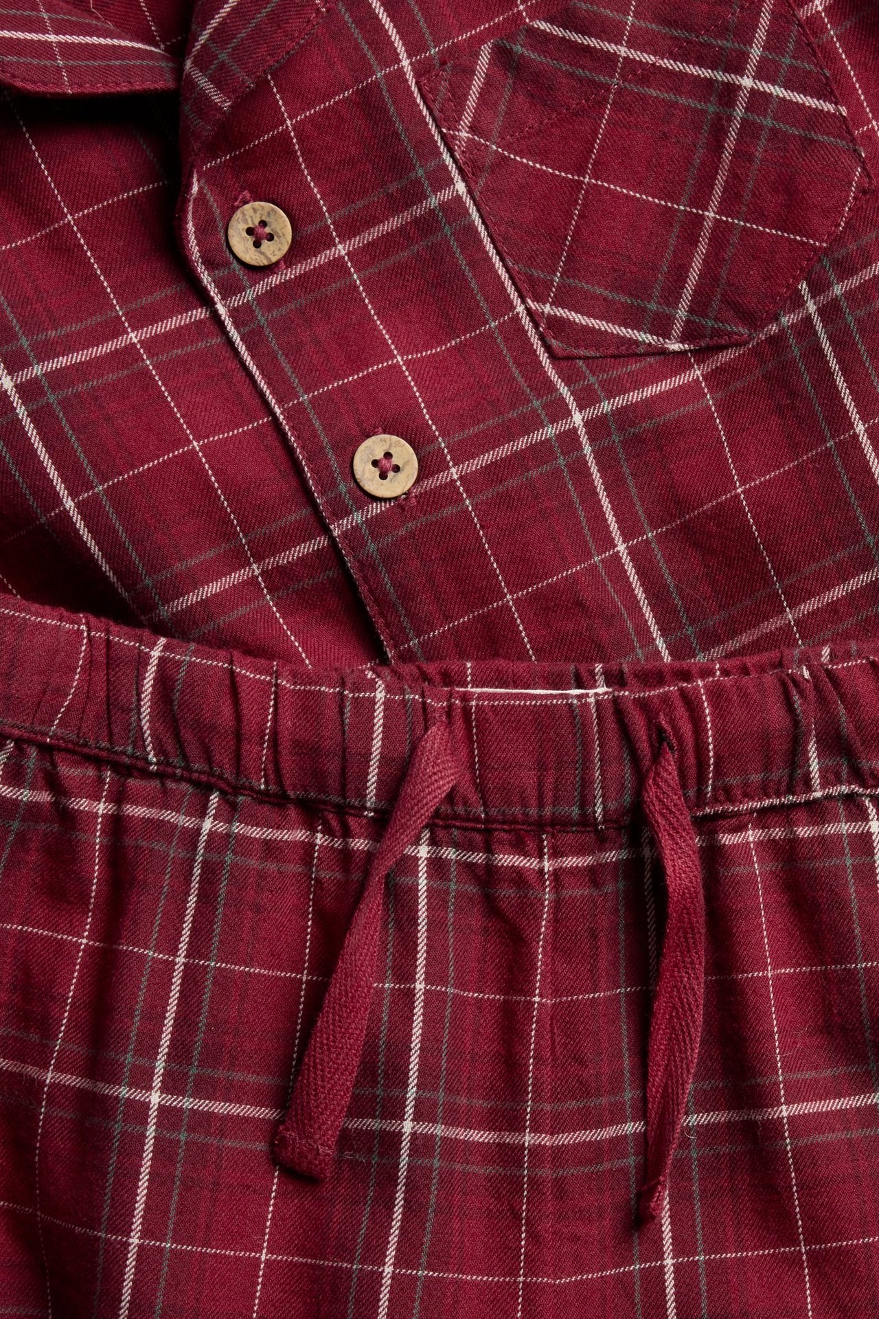 Nahaufnahme eines roten karierten Flanellpyjamas mit Holzknöpfen am Oberteil und Kordelzug an der Hose.