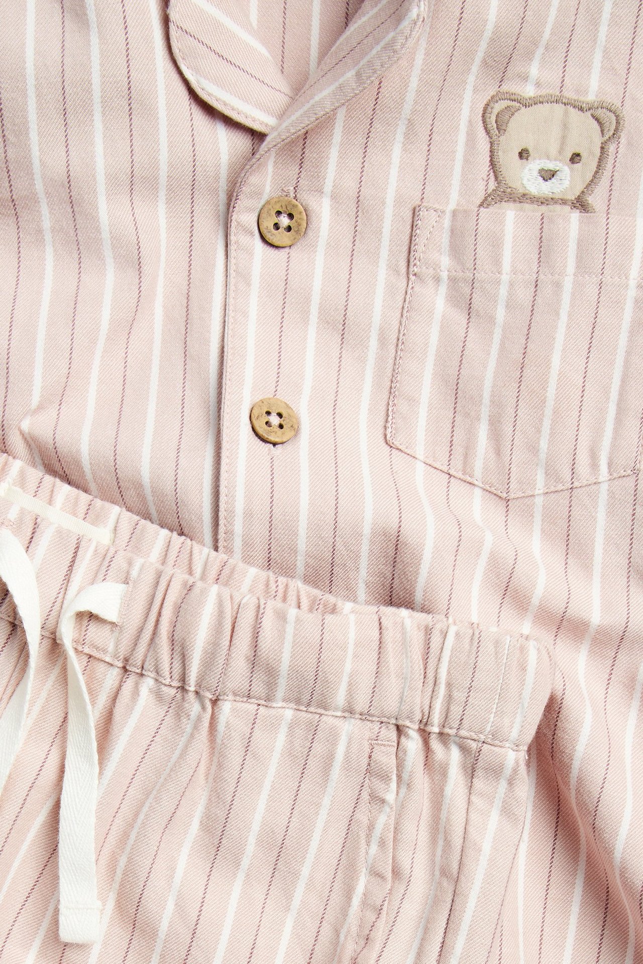 Nahaufnahme eines babyrosa gestreiften Baumwollpyjamas mit Holzknöpfen und Teddybär-Stickerei.