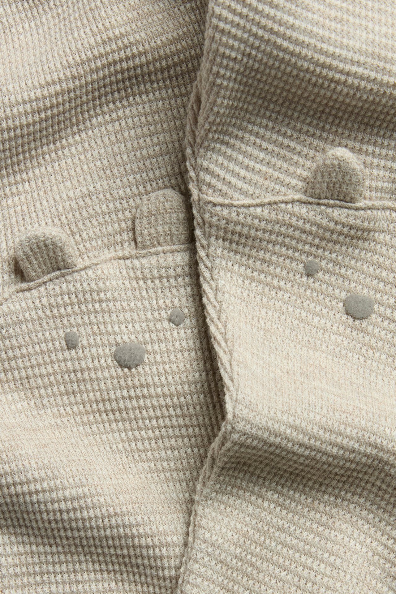 Nahaufnahme: beigemelierte Waffelstrick-Leggings mit Bärenohren und Gesichtern an den Knien.