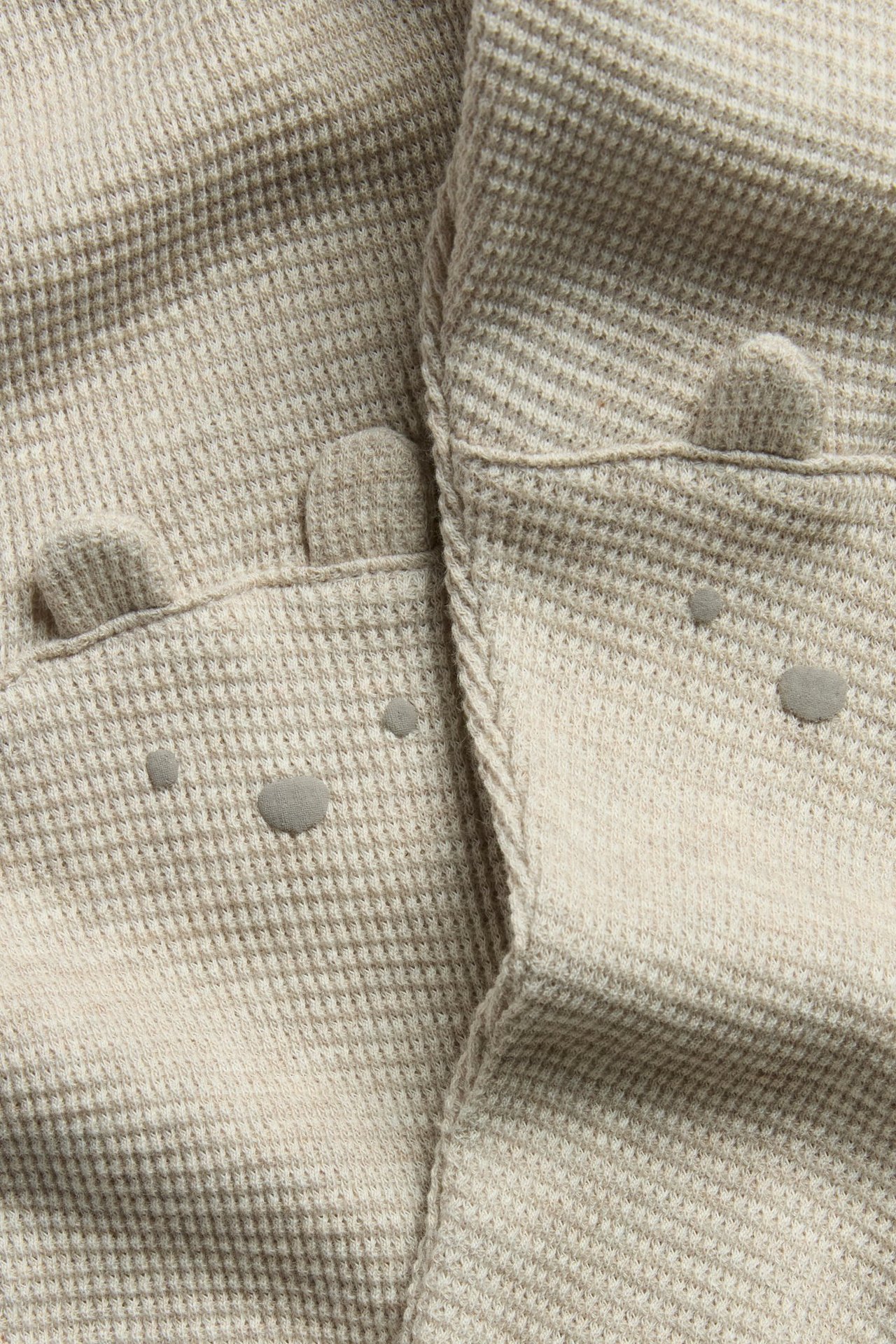 Nahaufnahme: beigemelierte Waffelstrick-Leggings mit Bärenohren und Gesichtern an den Knien.