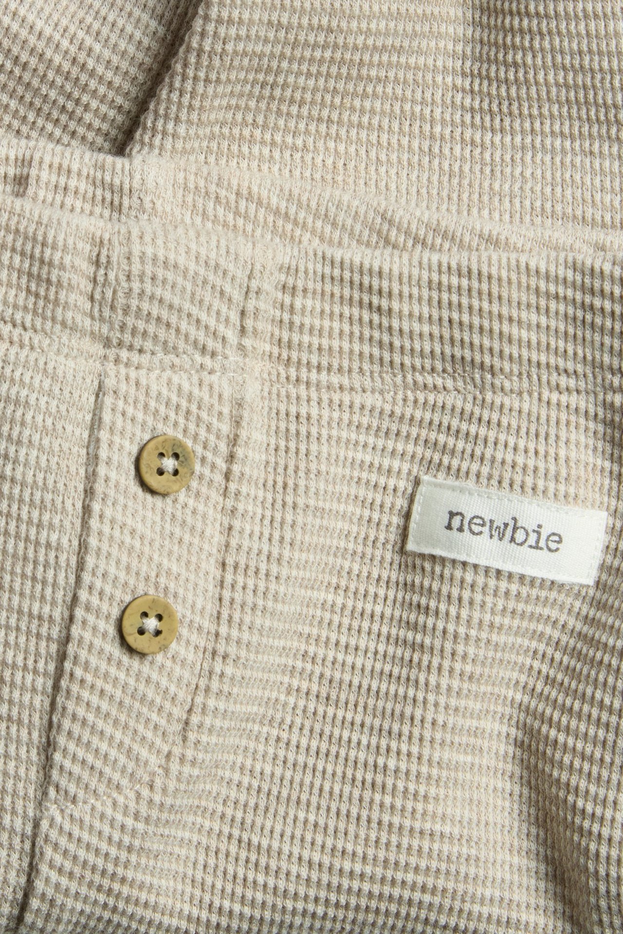 Nahaufnahme von beigemelierte Waffelstrick-Leggings mit zwei Zierknöpfen und einem 'newbie'-Etikett.