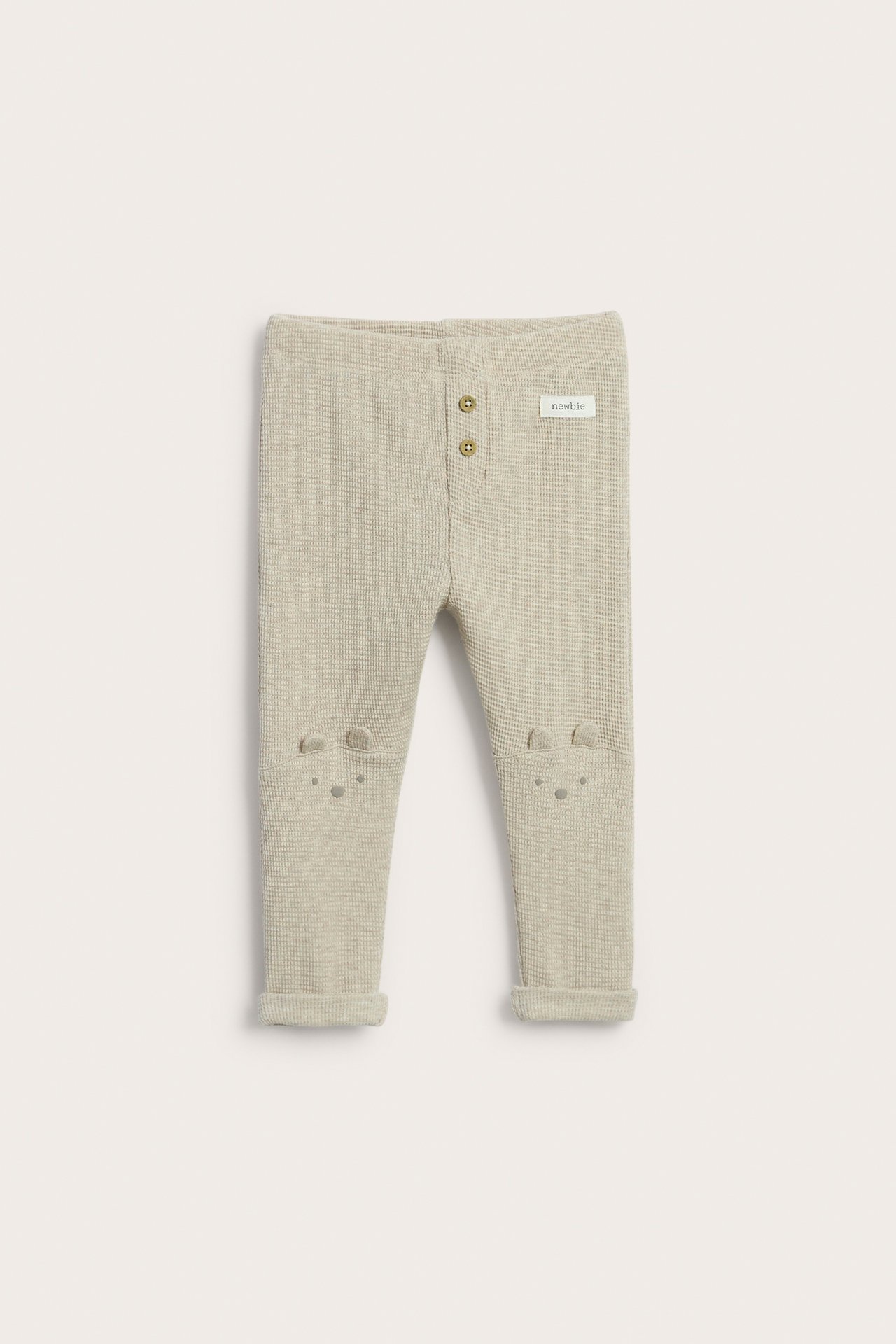 Vorderansicht: Hellbeige Baby-Waffel-Leggings mit Zierknöpfen, gestickten Knieohren und umgeschlagenen Beinen.