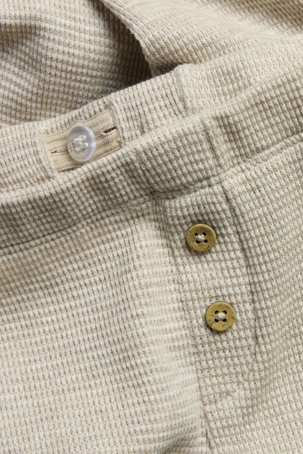 Nahaufnahme beigefarbener Melange-Waffel-Leggings mit dekorativen braunen und transparenten Knöpfen.