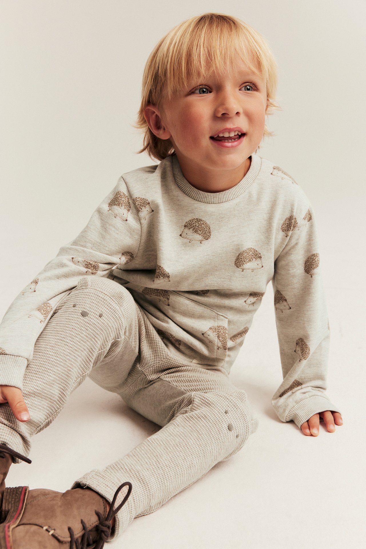 Front view: Kid's beige waffle-knit leggings with knee ears, dot print, and a grey hedgehog sweatshirt.