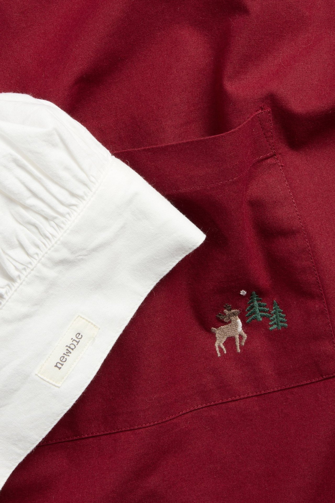 Nahaufnahme einer roten Baumwollschürze mit Rentierstickerei und einer weißen gerafften Bäckerhaube.