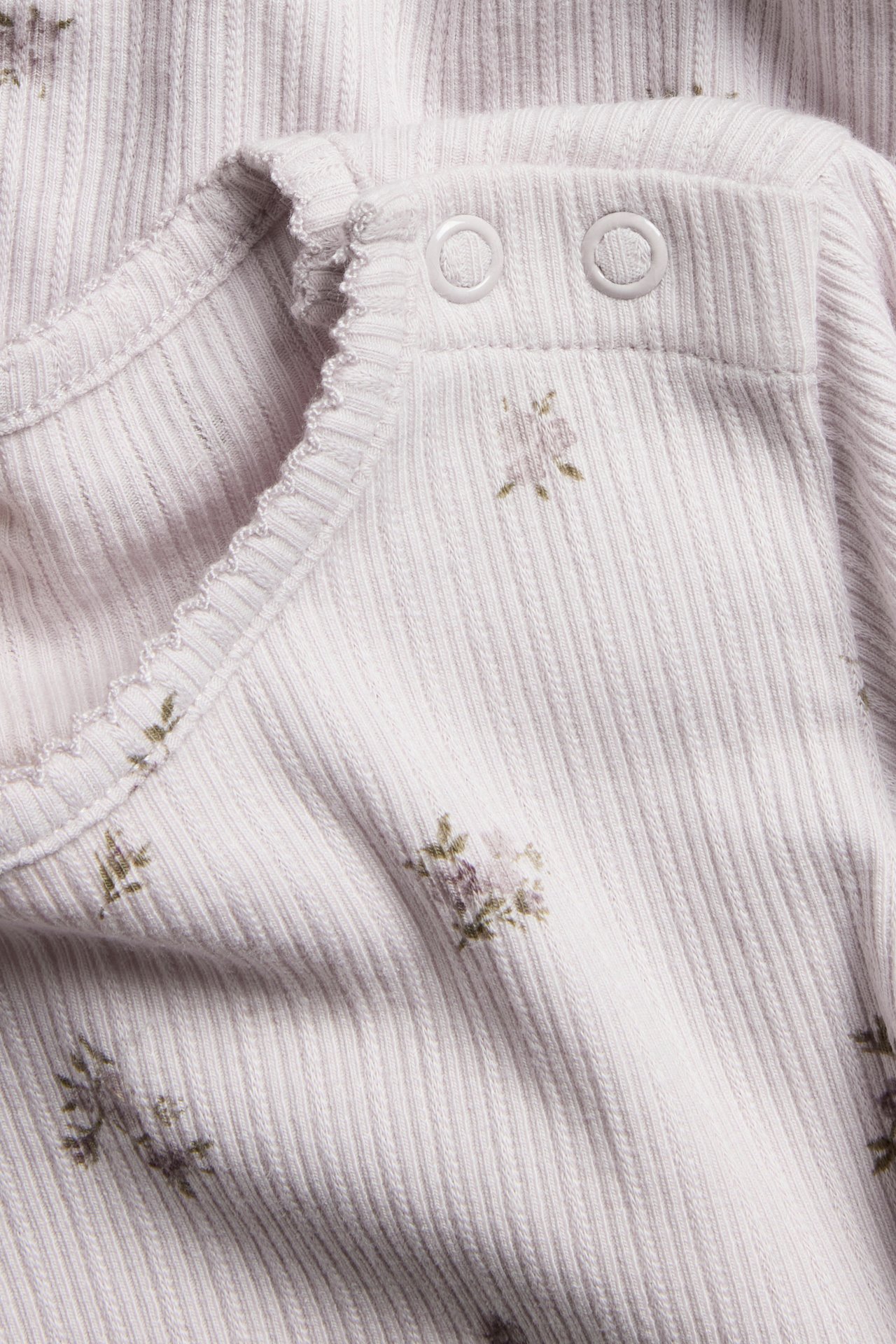 Close-up of a light lilac ribbed baby bodysuit with a floral print, picot neckline, and snap fasteners.