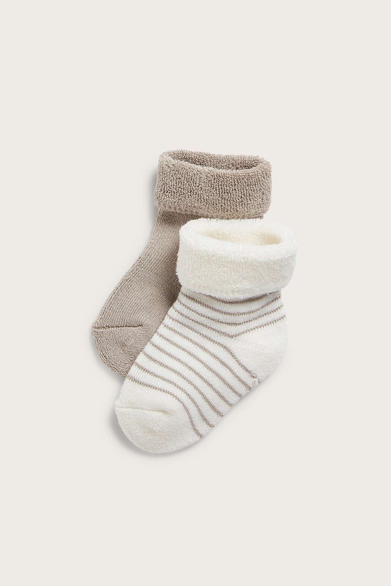 Close-up of two pairs of baby terry socks: one striped off-white, one solid beige, both with folded cuffs.