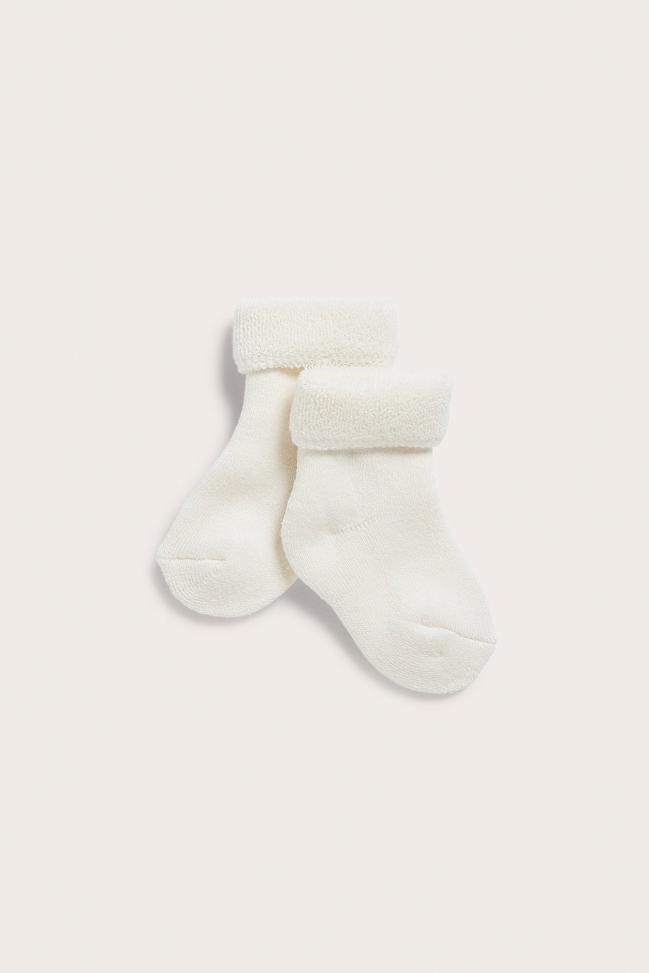 Vorderansicht von zwei cremeweißen Frottee-Babysocken mit umgeschlagenen Bündchen.