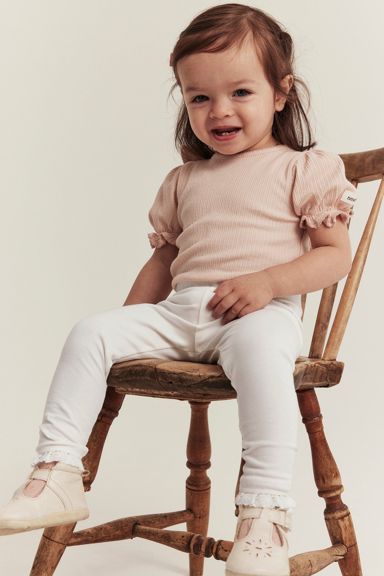 Front view of a kid wearing offwhite jersey leggings with lace cuffs, a pink ribbed top, and beige shoes.