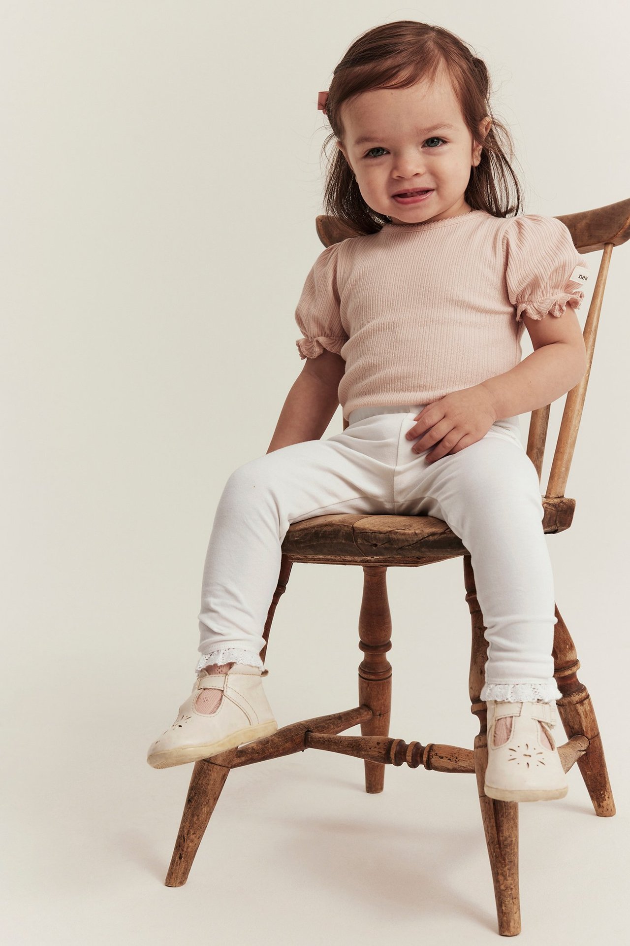 Front view: baby wearing off-white cotton leggings with lace trim, a pink ribbed top, and light shoes.