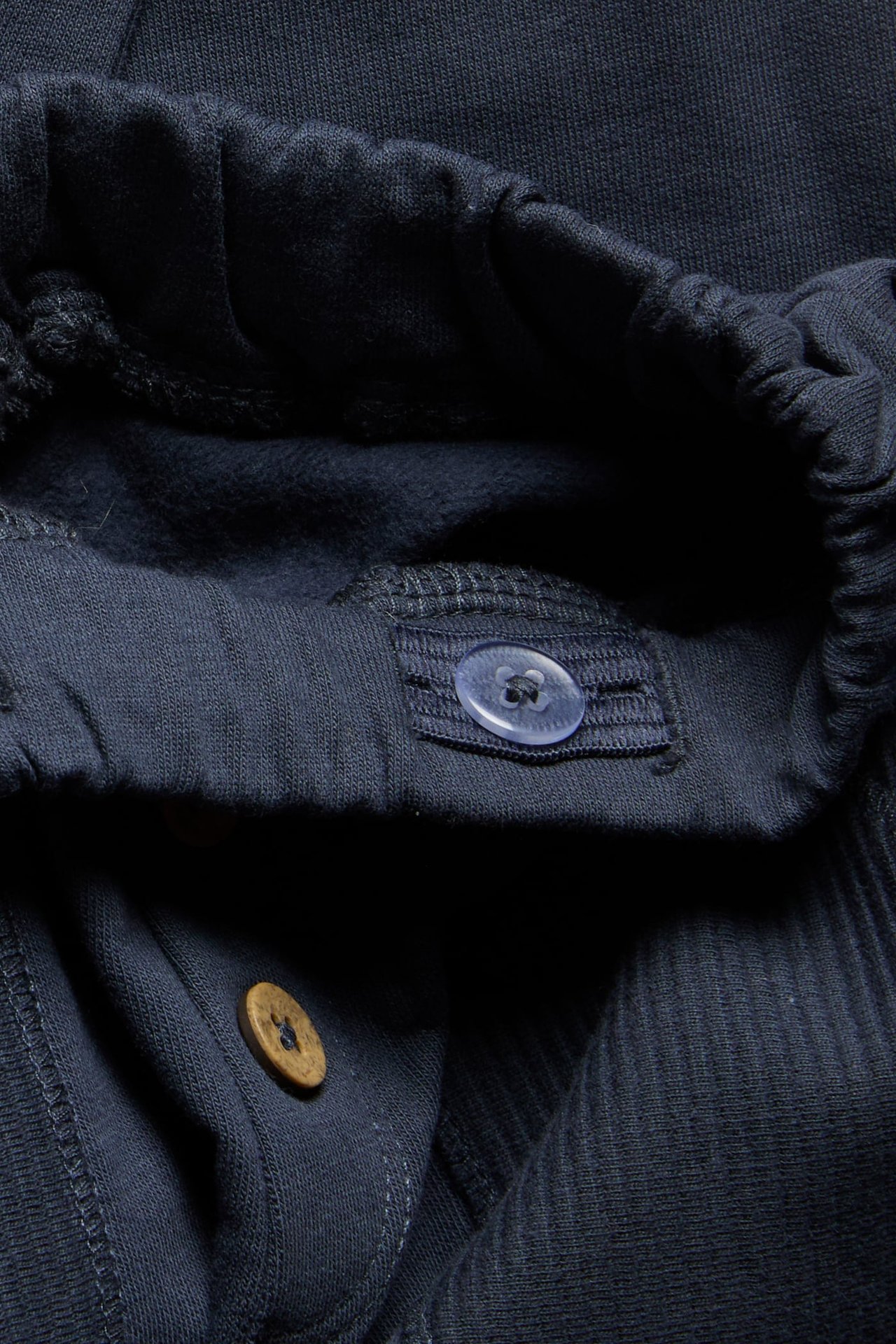 Close-up of dark blue cotton jogging trousers with adjustable elastic waist and decorative buttons.