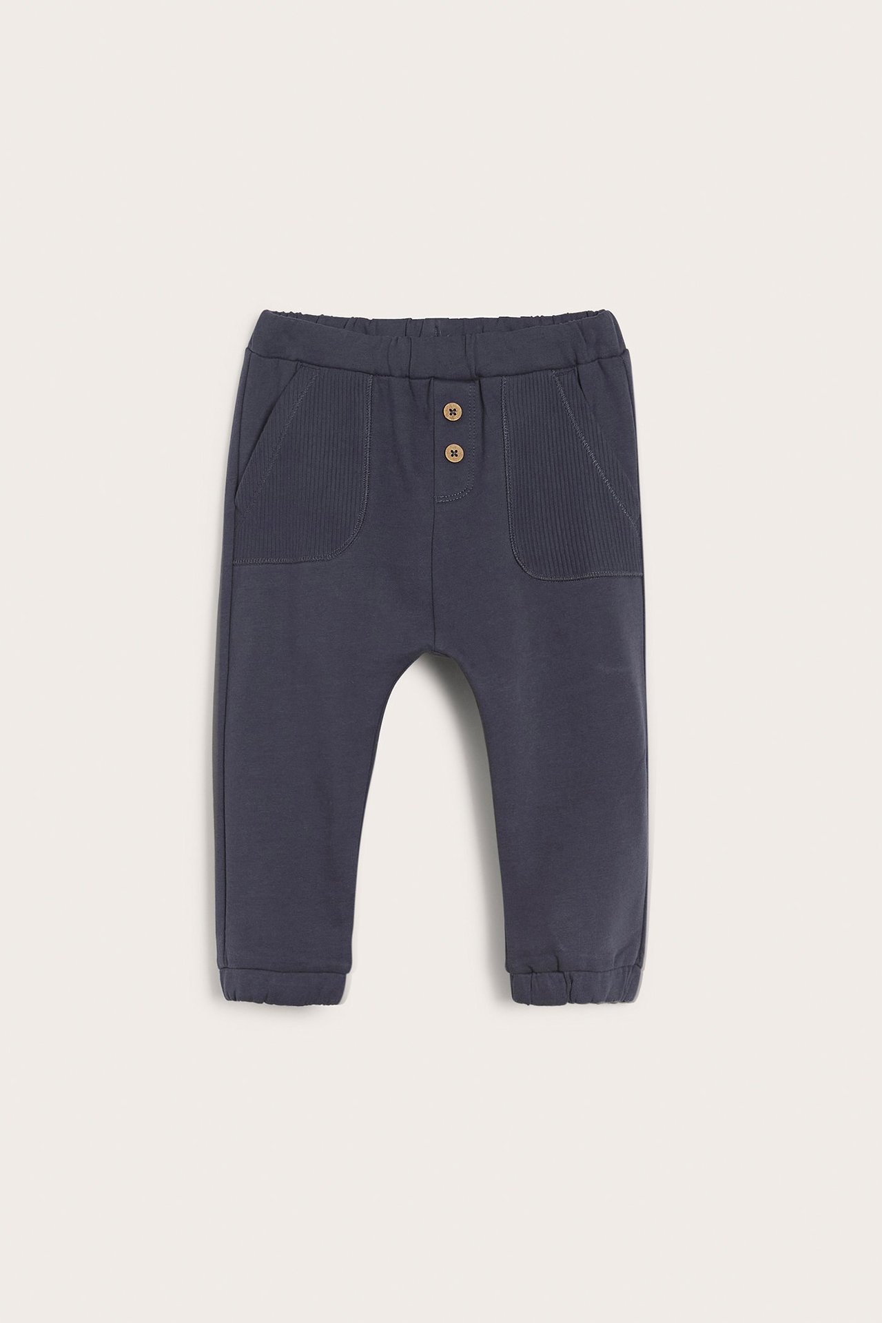 Front view of dark blue cotton baby jogging pants with an elasticated waist, two decorative buttons, and ribbed front pockets.