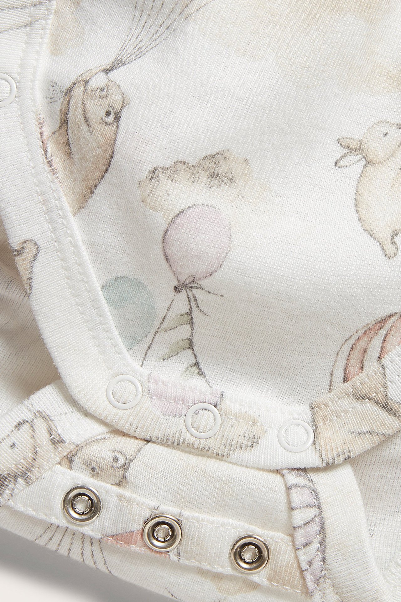 Close-up of an off-white cotton baby bodysuit with animal and balloon print, featuring snap buttons.