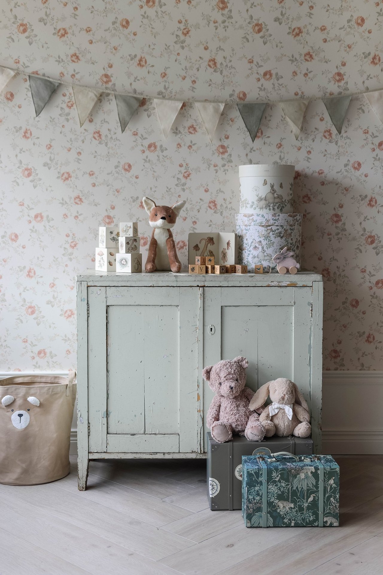 Vorderansicht: Eine hellbeige und graue Baumwollwimpelkette hängt in einem Raum mit Schrank, Stofftieren und Aufbewahrung.