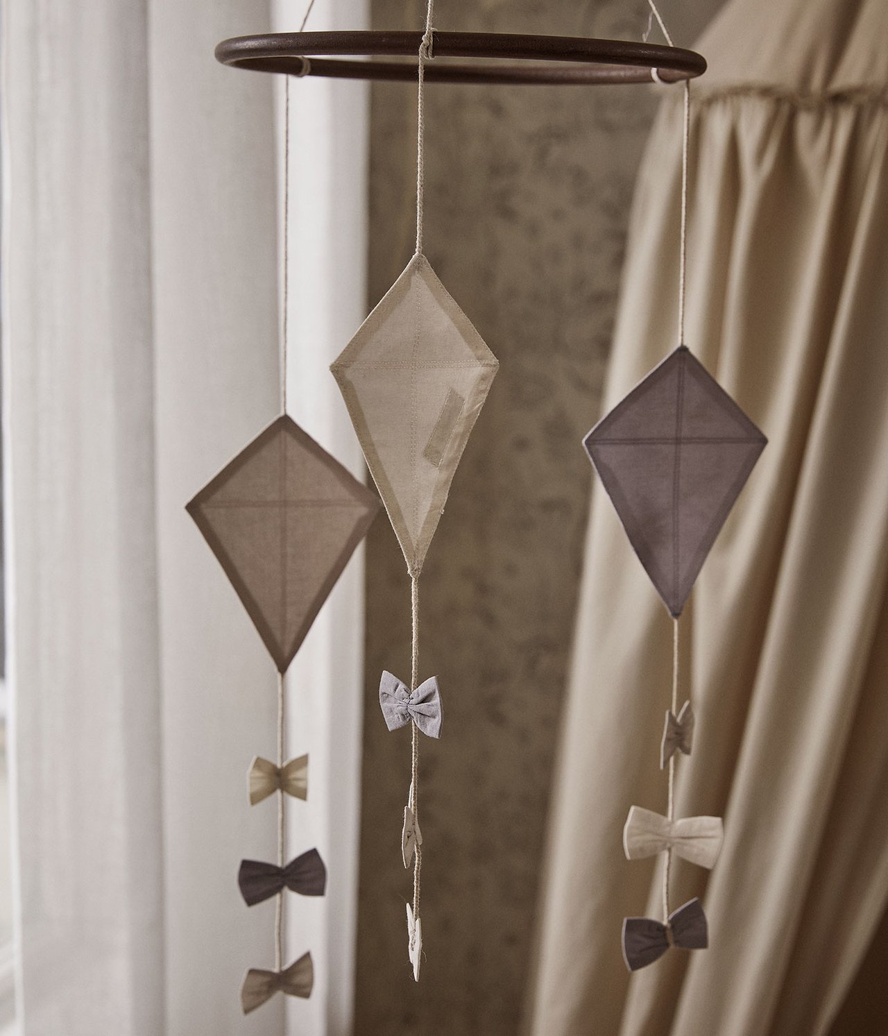Close-up of a baby mobile with a wooden ring, light beige and brown fabric kites, and small bows.