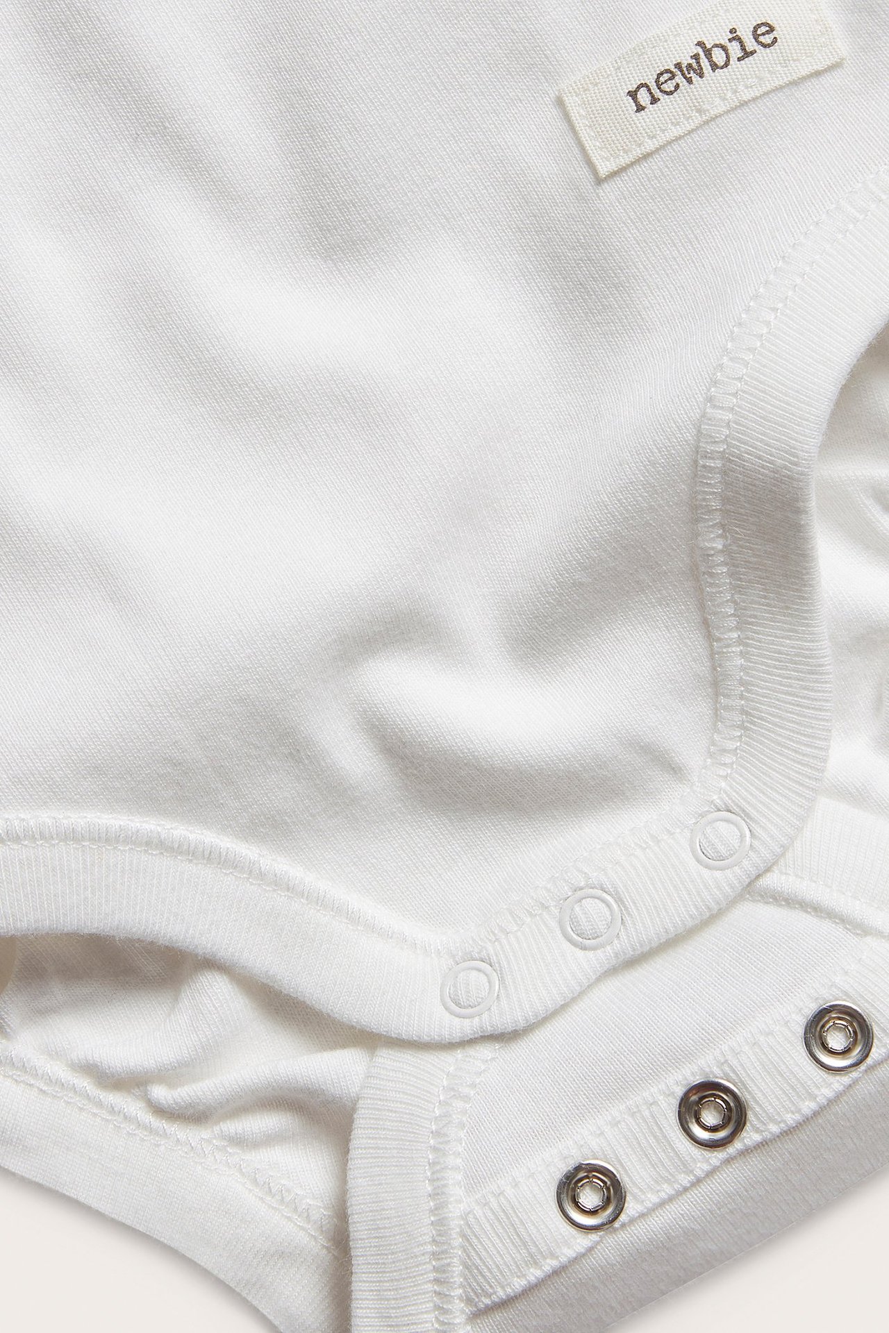 Close-up of an off-white cotton baby bodysuit with snap buttons at the shoulder and crotch.