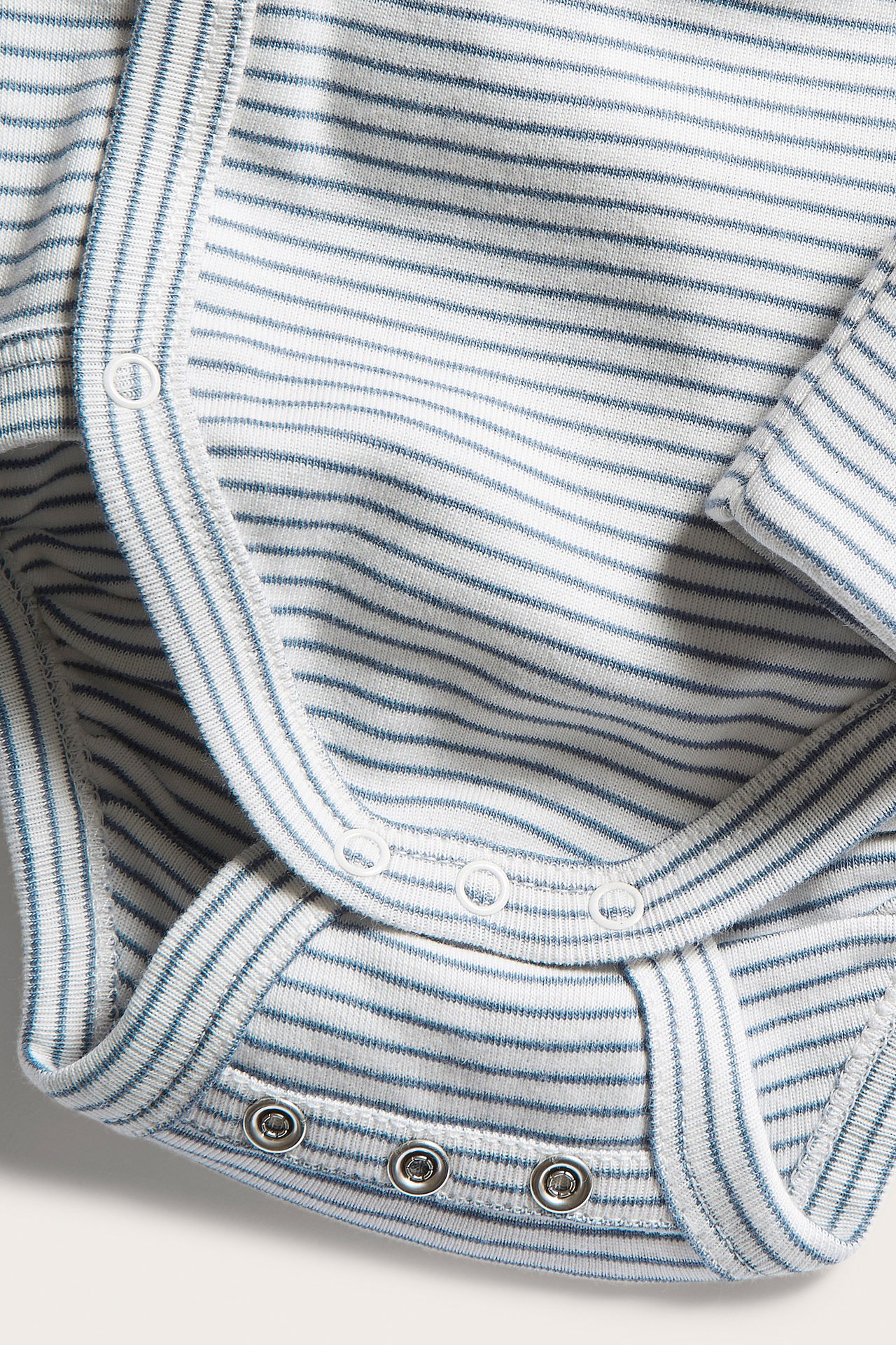 Close-up of a blue and white striped organic cotton baby wrap-style bodysuit with snap buttons.