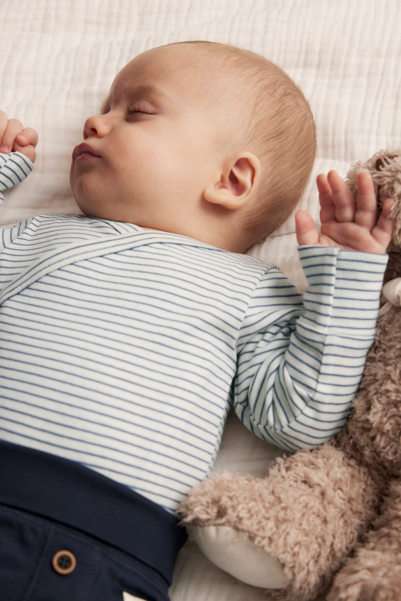 Close-up of a sleeping baby in a light blue striped long-sleeved cotton wrap-style bodysuit and dark blue pants.