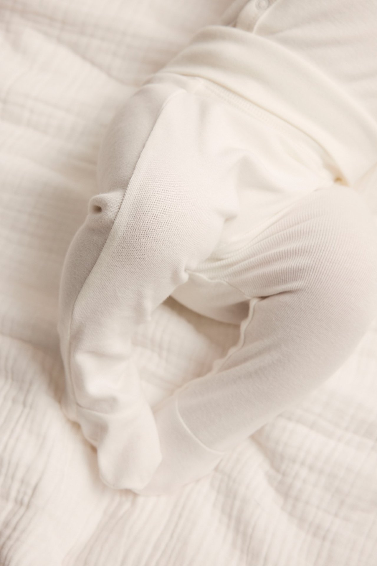 Close-up of a baby wearing solid off-white cotton footed leggings and a matching top.