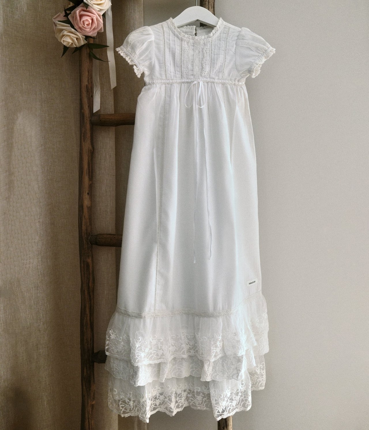 Front view of an offwhite baby christening gown with short puffed sleeves, lace trim, pintucks, and ruffled lace hem.
