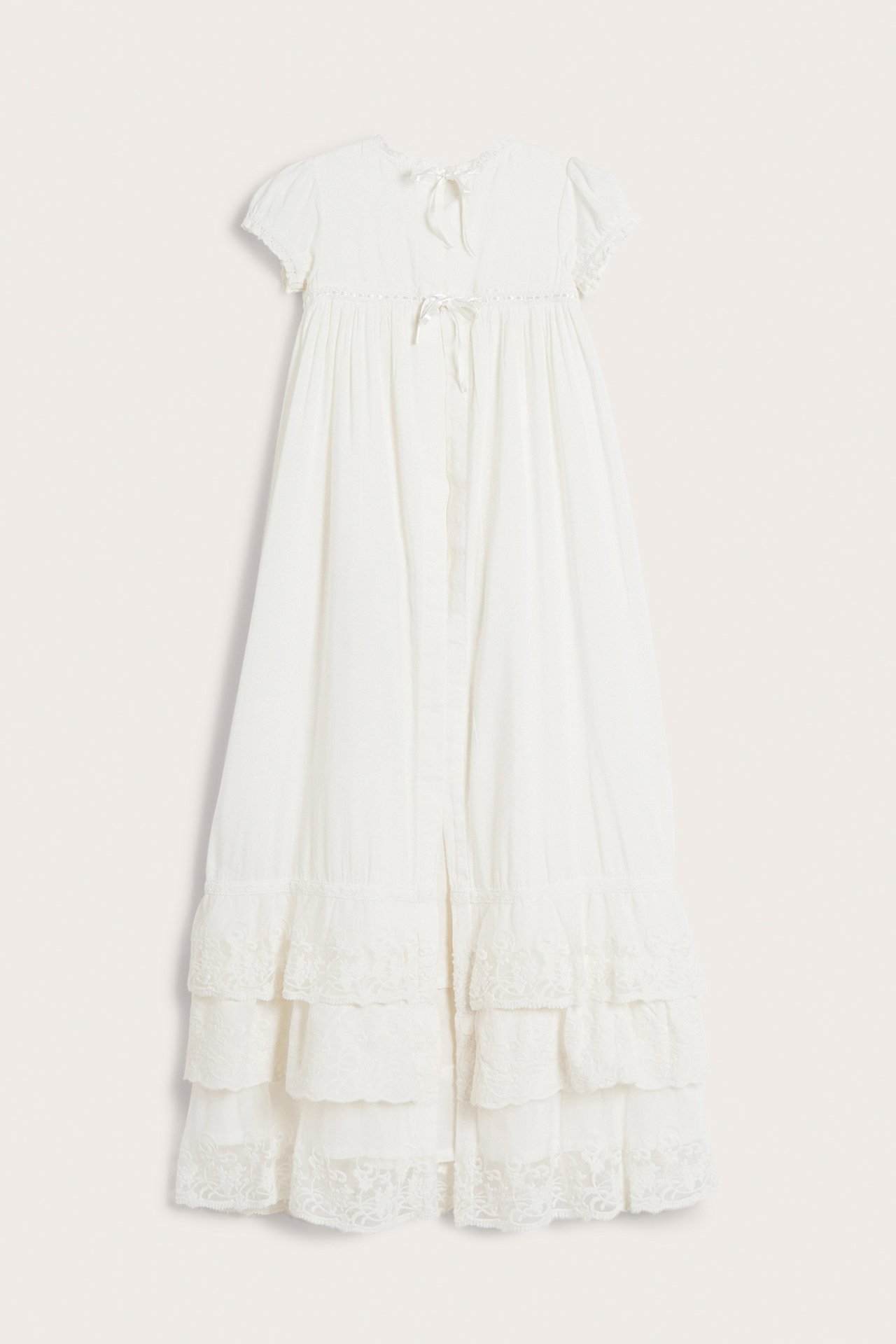 Front view of an off-white baby christening gown with short sleeves, back ties, and ruffled lace-trimmed tiers.