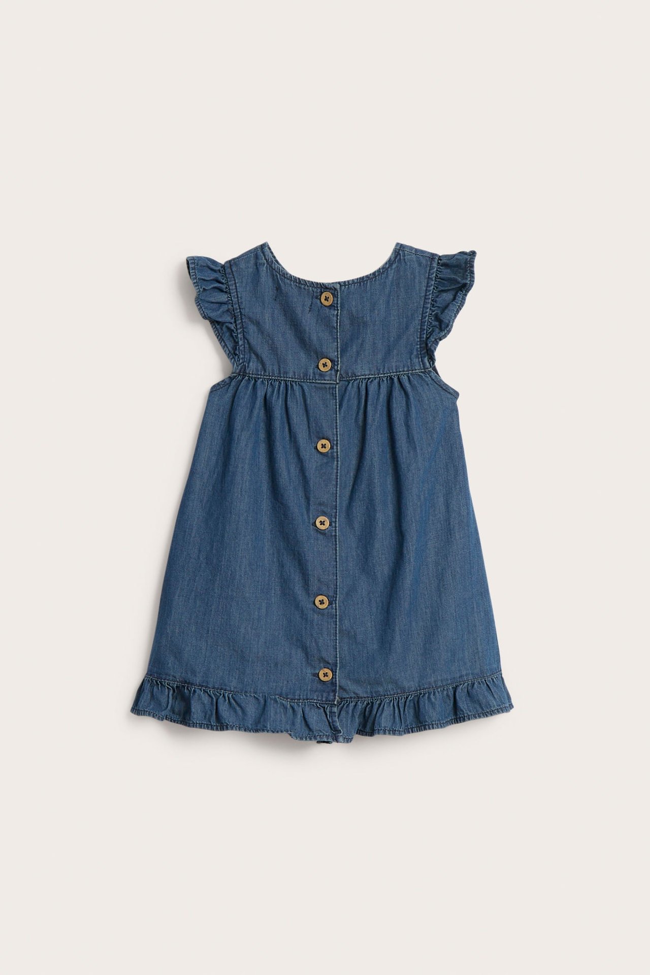 Back view: Baby's blue denim dress with ruffled shoulders, ruffled hem, coconut buttons.