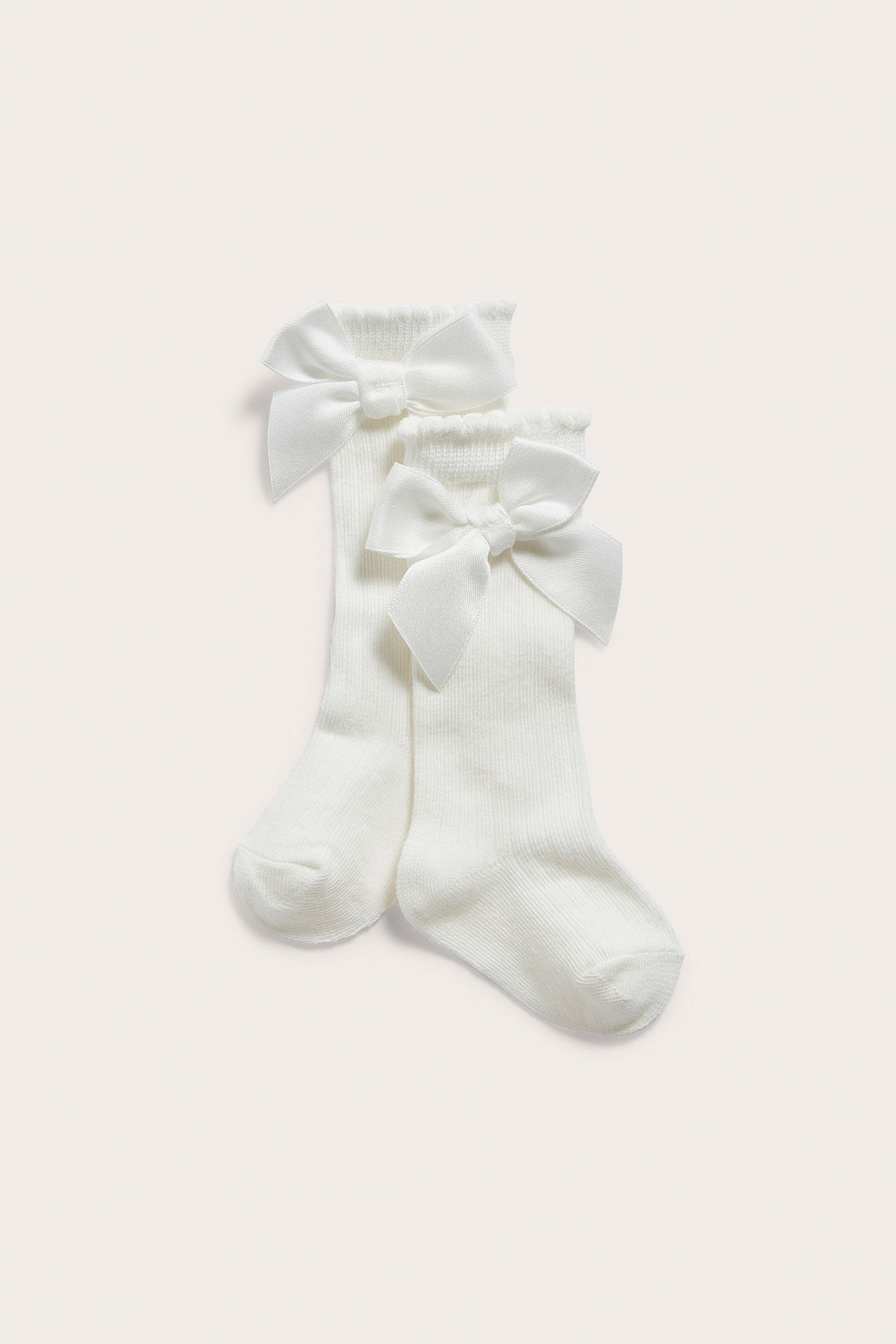 Front view of offwhite rib-knitted knee-high socks for kids, each with a decorative bow on the cuff.