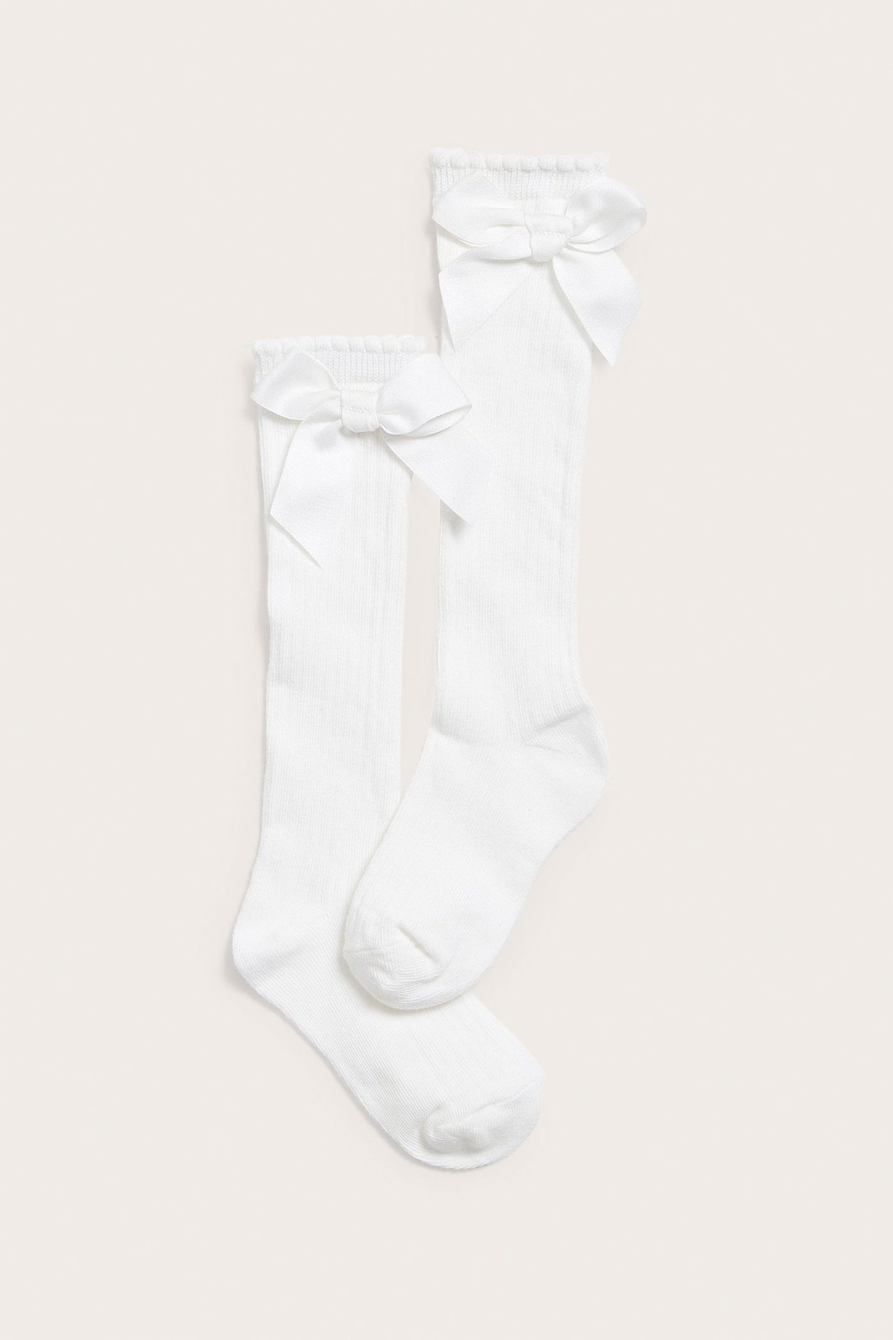 Draufsicht auf zwei cremefarbene gerippte Kniestrümpfe, jeweils mit einer dekorativen Schleife am oberen Rand.
