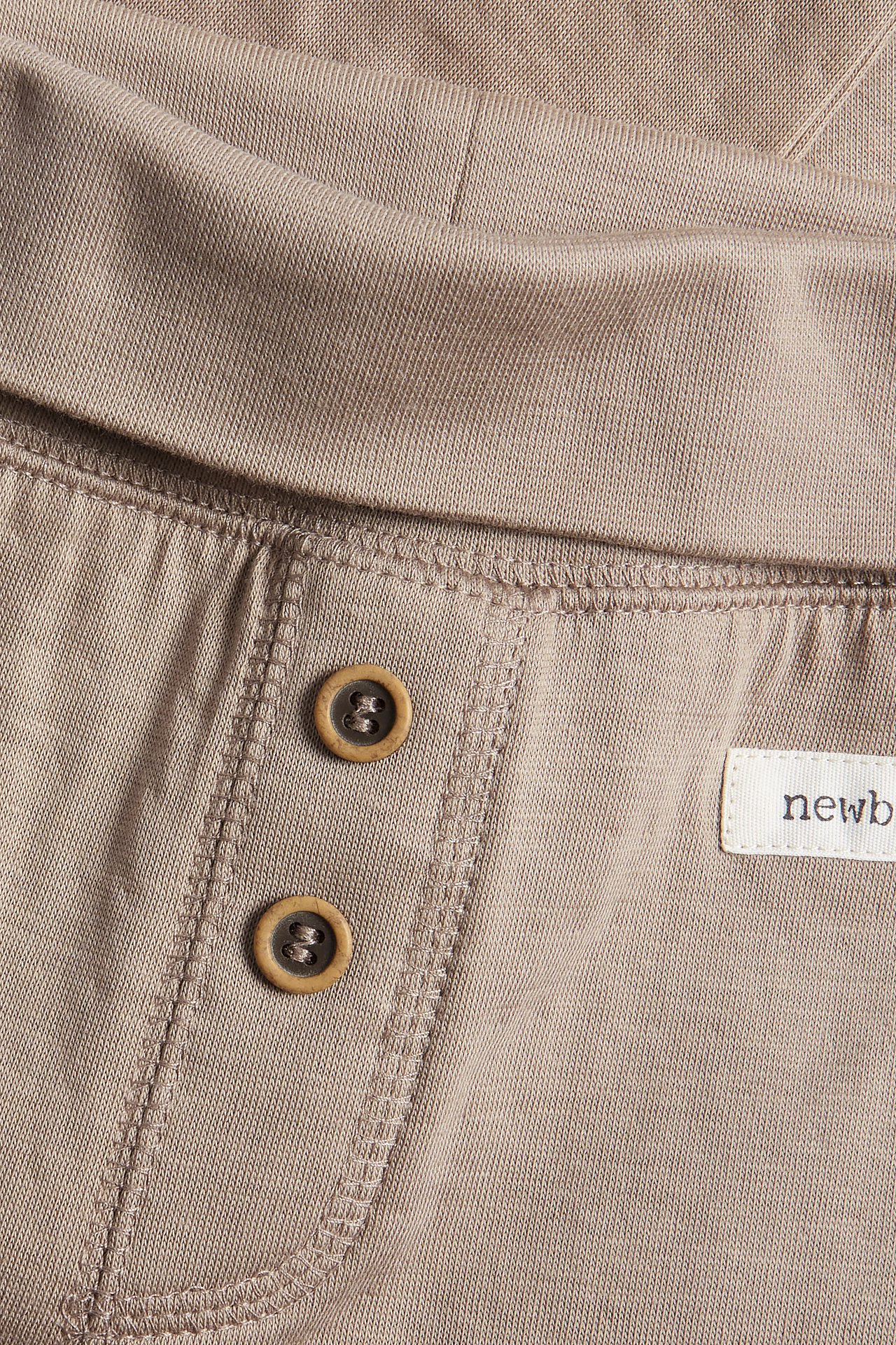 Nahaufnahme von beigen Baby-Baumwoll-Leggings mit umklappbarem Bund und zwei Zierknöpfen.