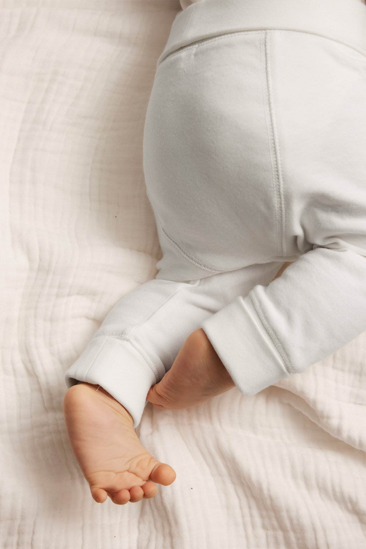 Nahaufnahme eines Babys in cremeweißen Baumwoll-Leggings mit umgeschlagenem Bund und Bündchen an den Knöcheln.