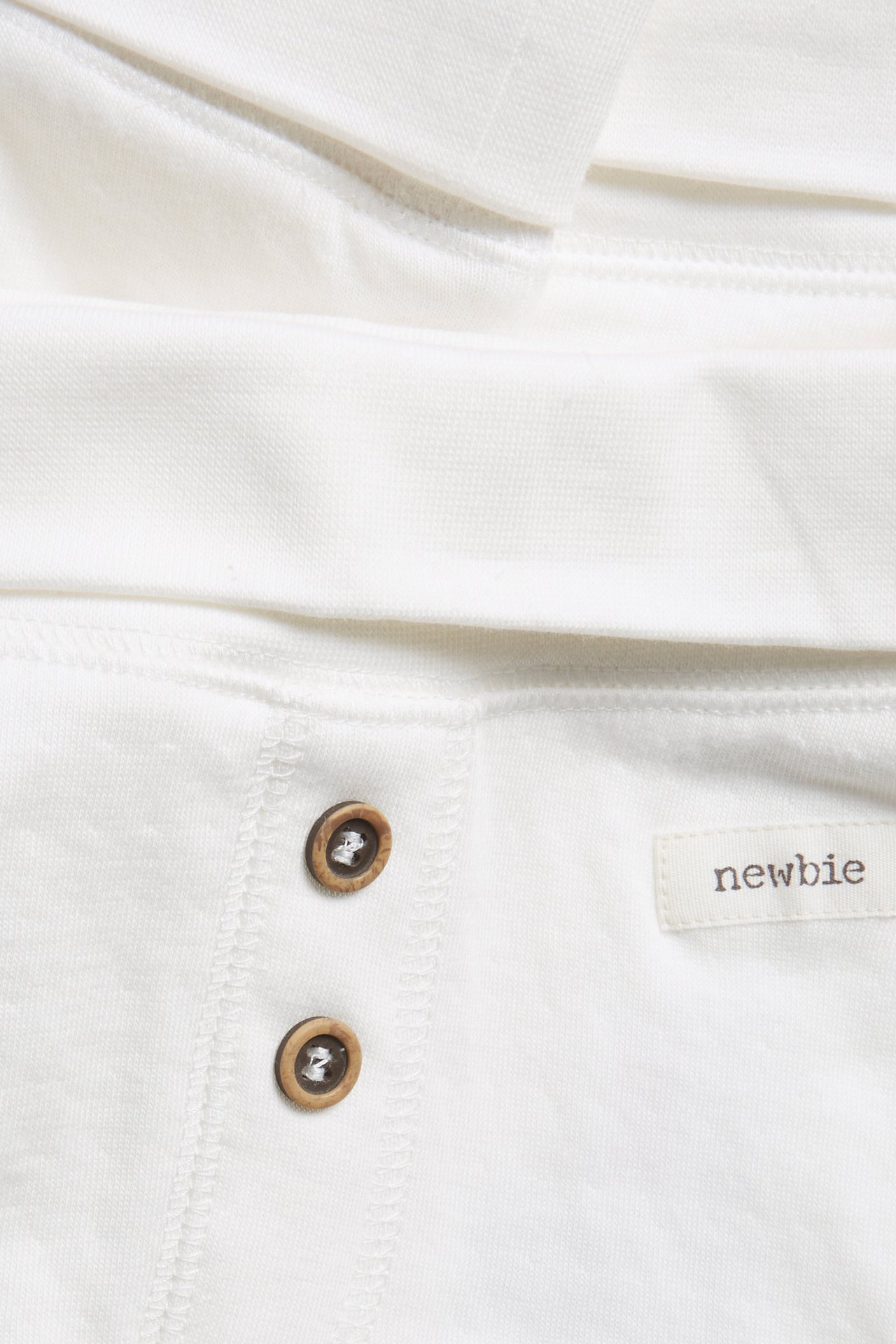 Close-up of off-white baby cotton leggings with folded waistband, two decorative wooden buttons, and a Newbie tag.