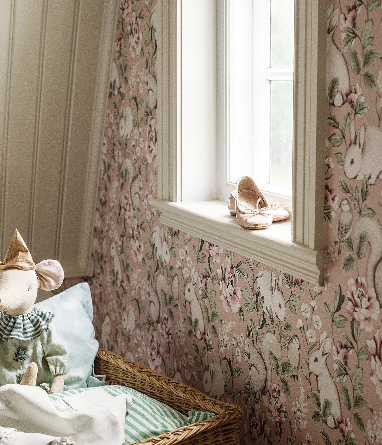 Rosa Vliestapete mit Kaninchen, Eichhörnchen und Blumen. Rosa Ballerinas auf Fensterbank, Maus-Spielzeug im Korb.