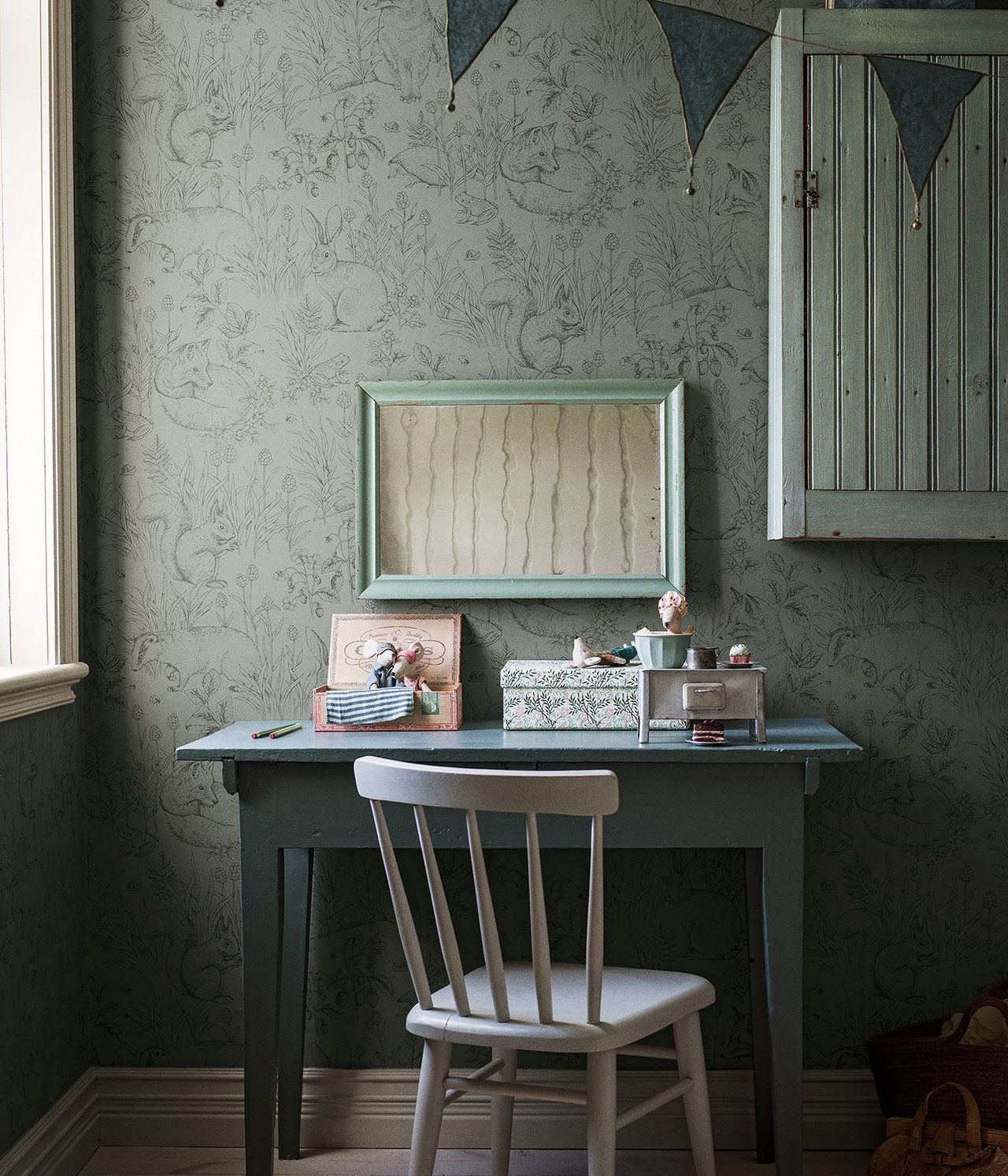 Vorderansicht: Grüne Vliestapete mit Tiermuster, ein grüner Schreibtisch und ein weißer Stuhl.
