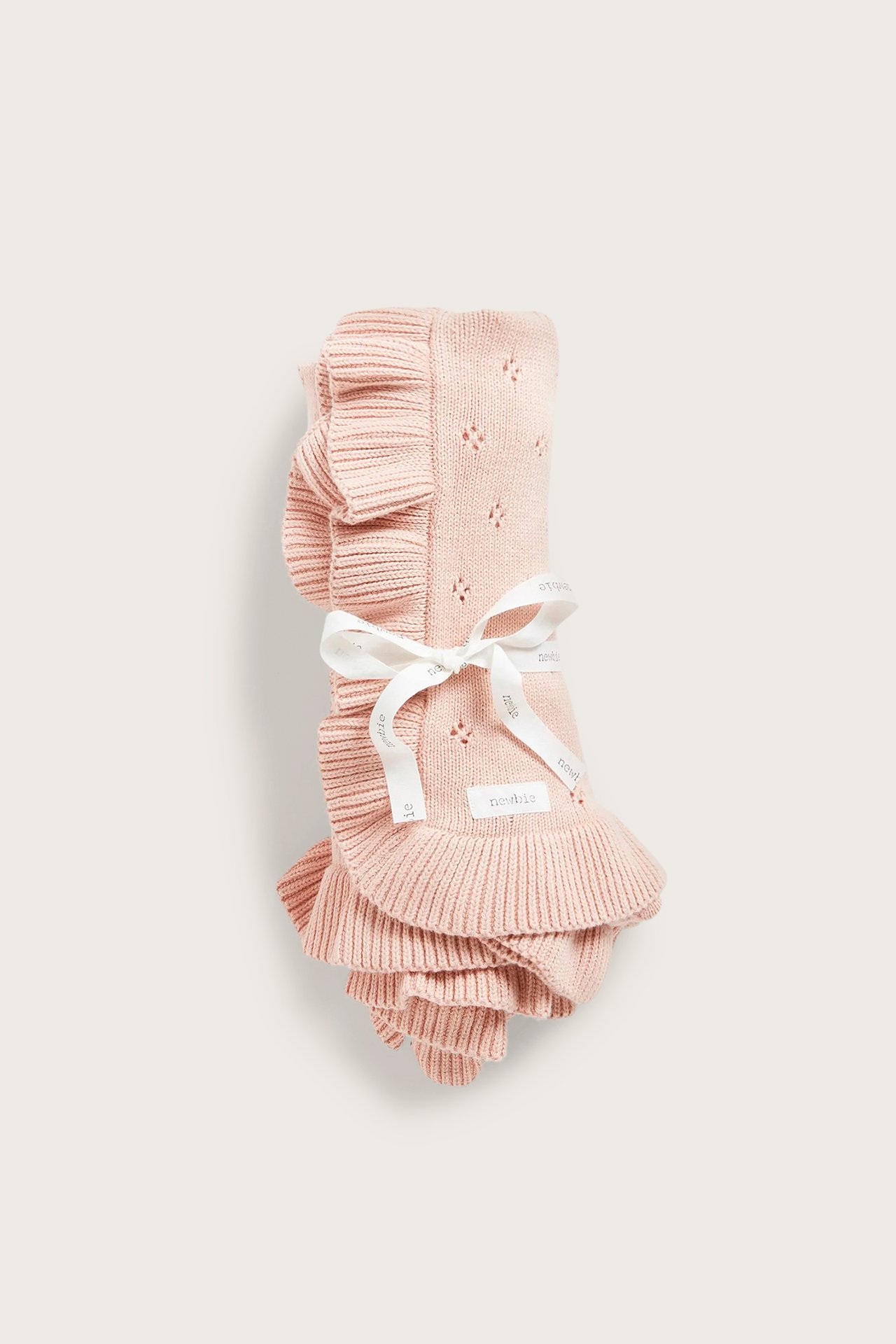 Front view: Light pink knitted organic cotton baby blanket with openwork pattern, ruffled edge, tied with a white ribbon.