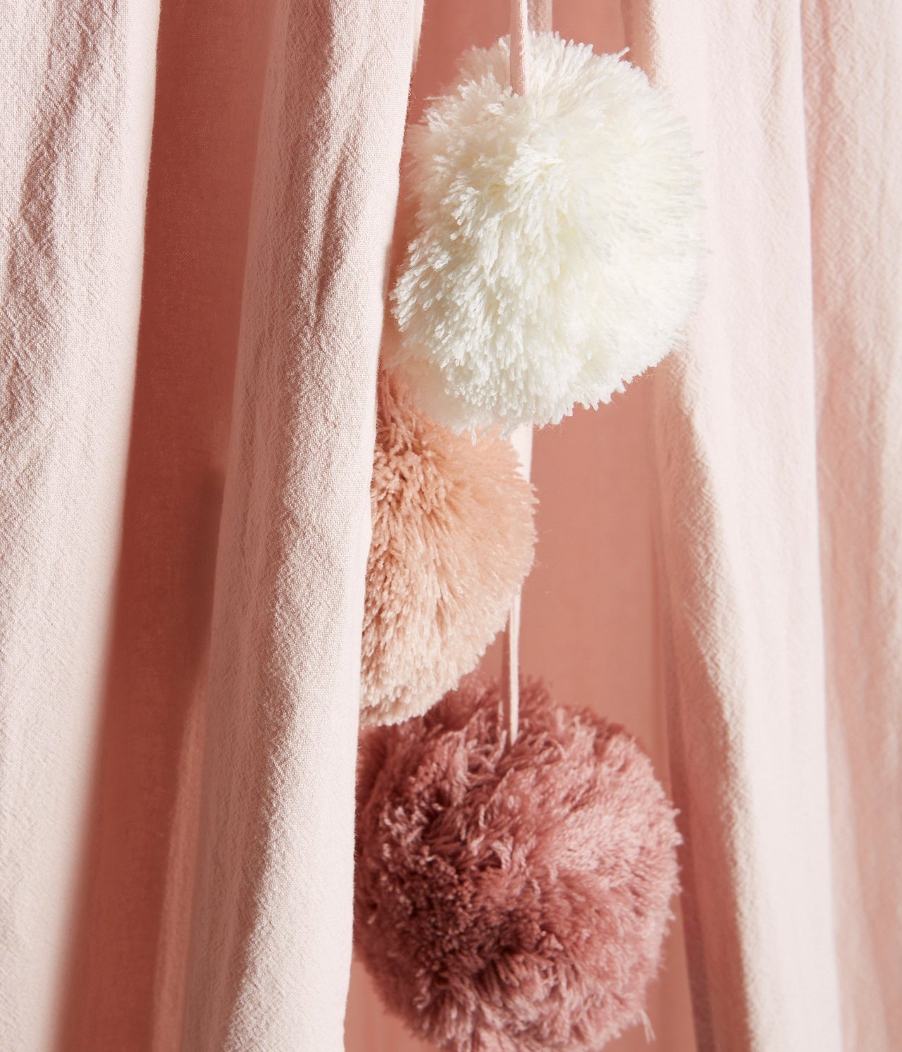 Nahaufnahme von rosa Lesetelt-Stoff mit drei hängenden Pompons in Weiß, Hellrosa und Dunkelrosa.