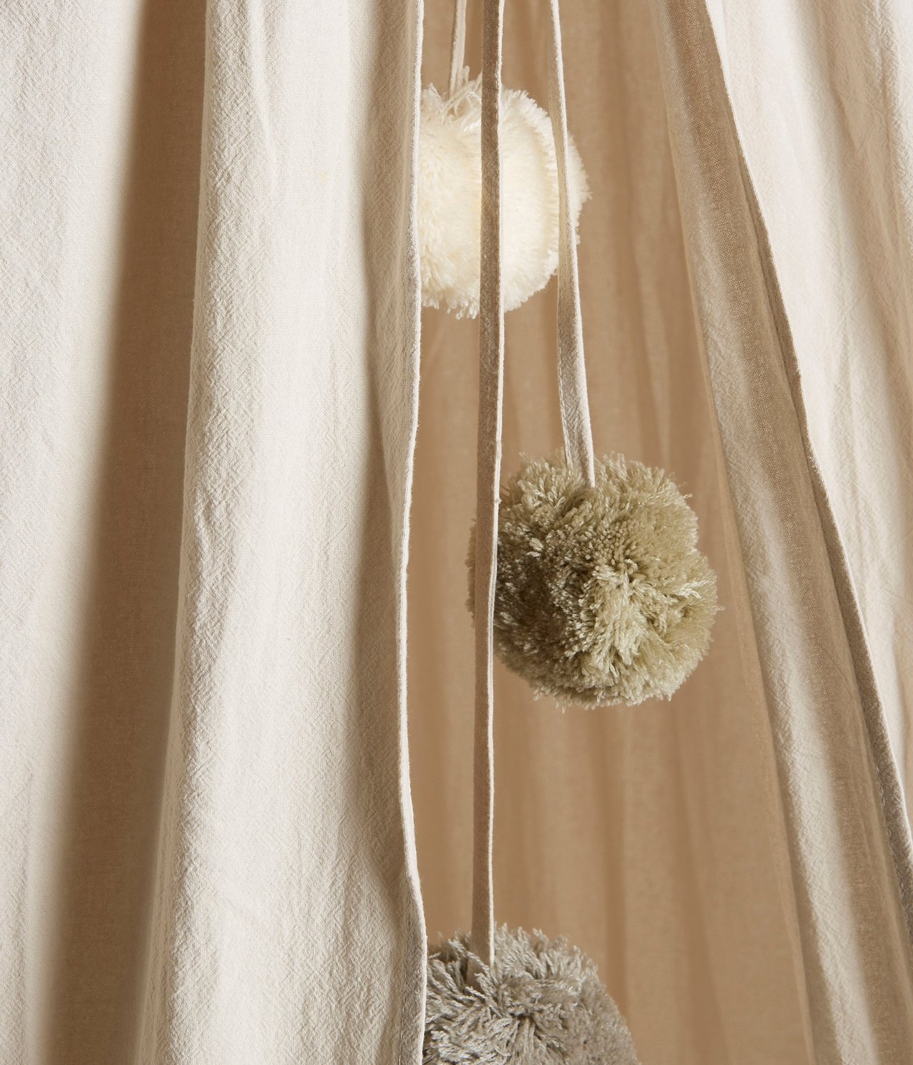 Nahaufnahme eines hellbeigen Leselagers mit hängenden mehrfarbigen Pompons.