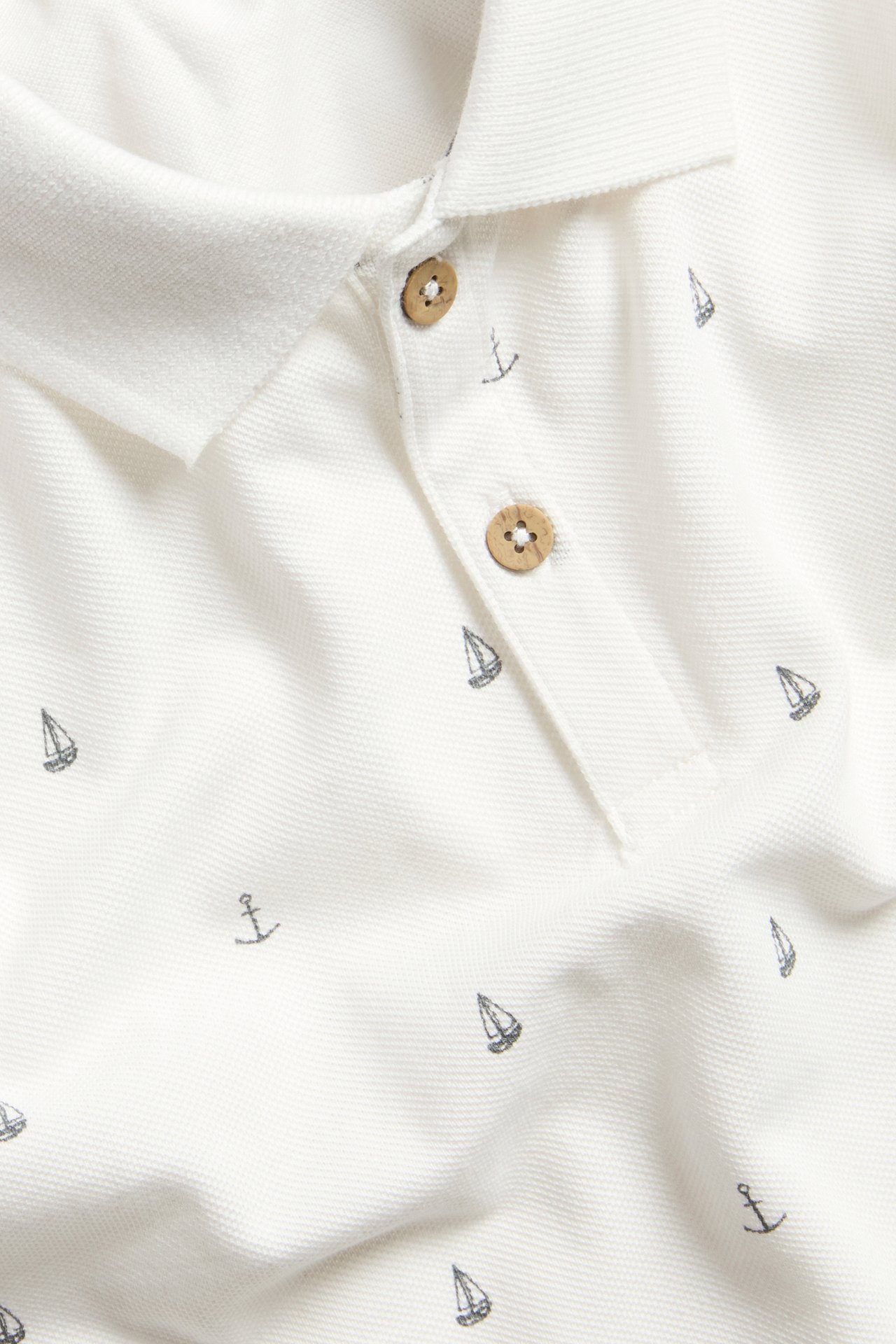 Close-up of an off-white kid's cotton polo shirt with a collar, wooden buttons, and a marine print.