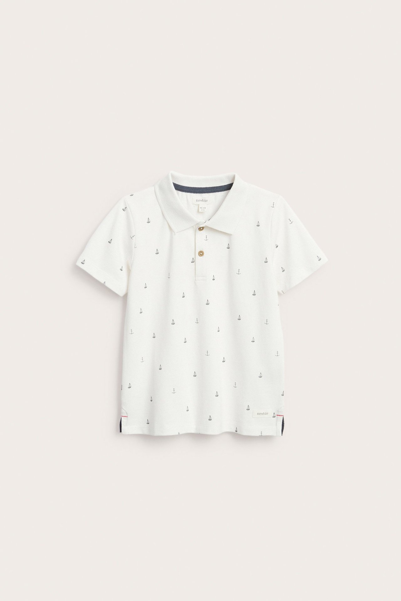 Front view of a kid's off-white cotton polo shirt with dark anchor print, three-button placket.