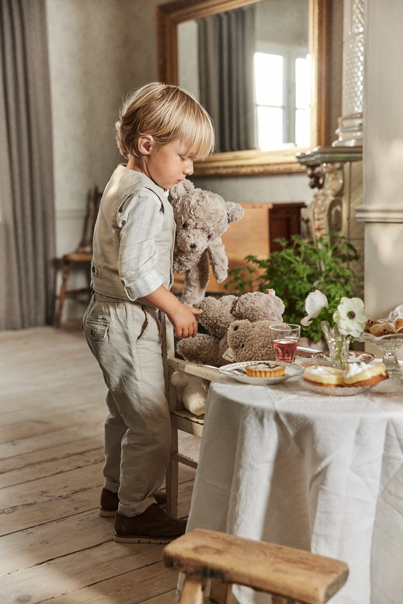Side view of a kid wearing beige woven trousers, a light beige vest, and a light plaid shirt.
