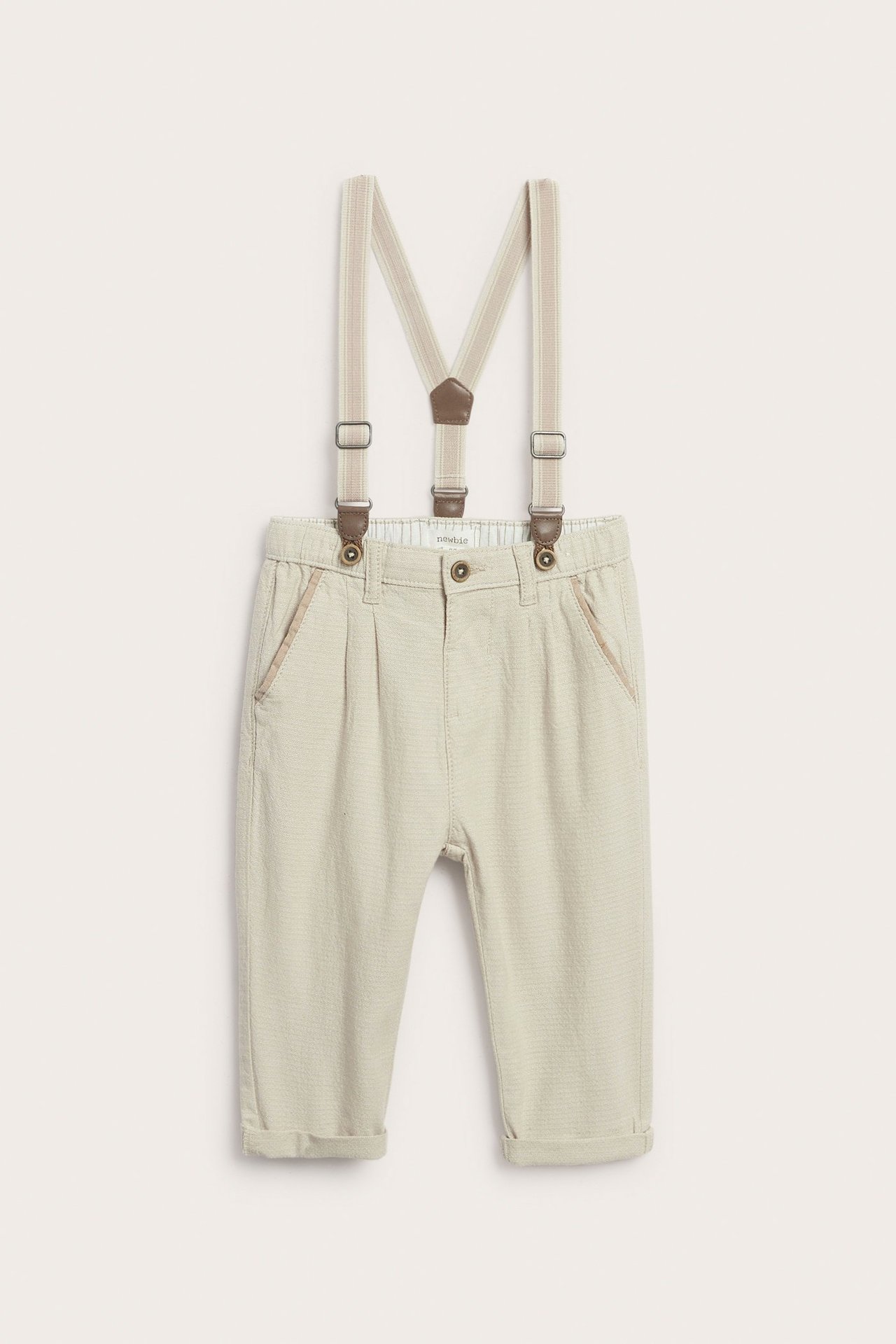 Vorderansicht: Beige gewebte Kinderhose mit verstellbaren beigen Hosenträgern und hochgekrempelten Bündchen.