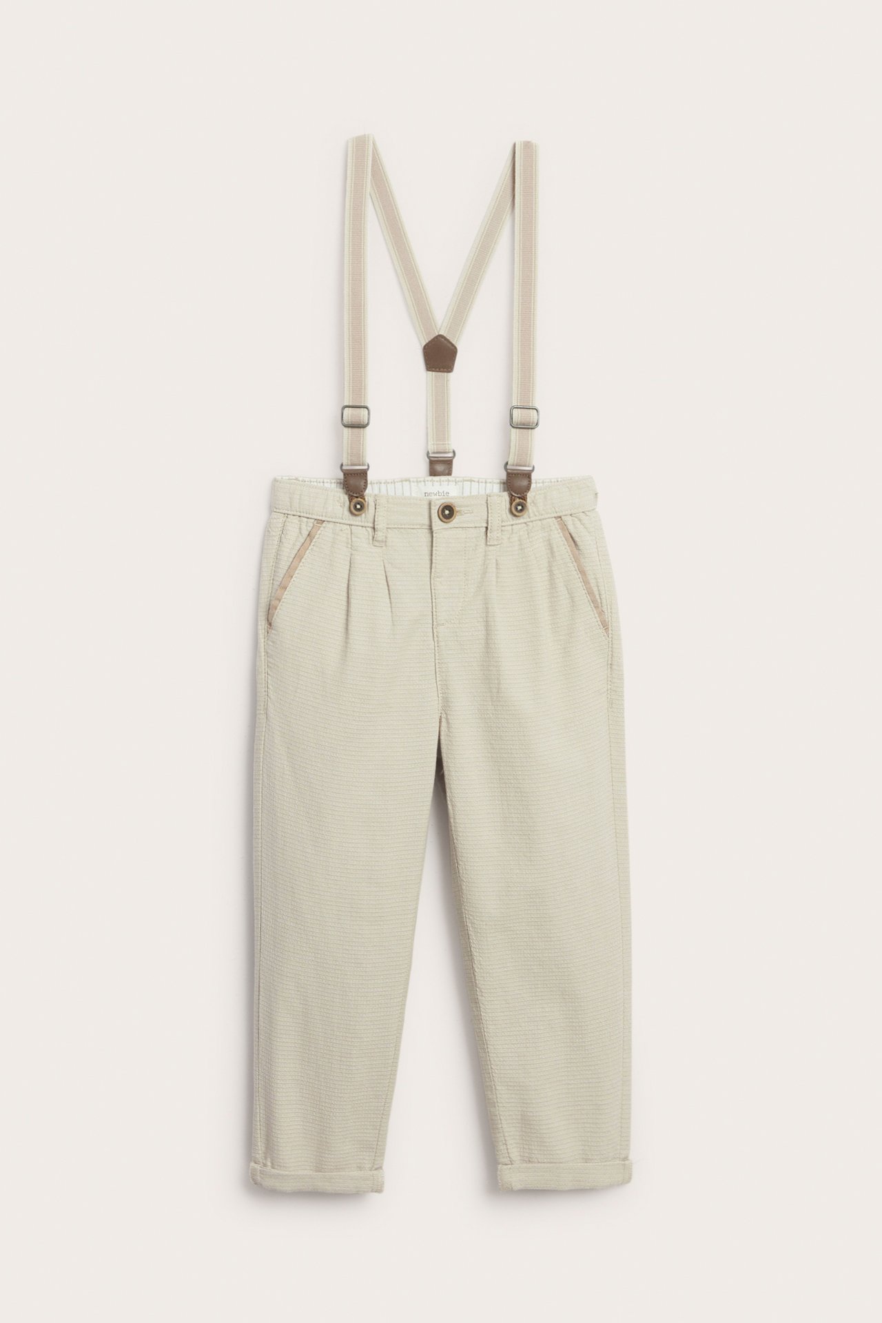 Front view of beige woven kid's trousers with adjustable suspenders, front button, and rolled-up legs.