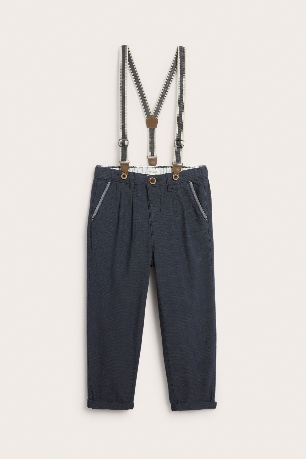 Front view of kid's dark blue woven cotton trousers with adjustable striped suspenders and cuffed legs.