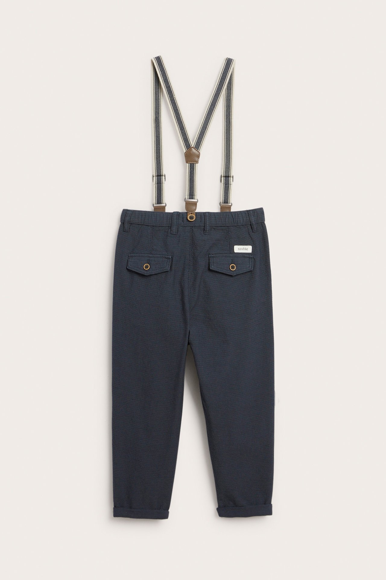 Front view of kid's dark blue woven cotton pants with rolled cuffs and striped adjustable suspenders.
