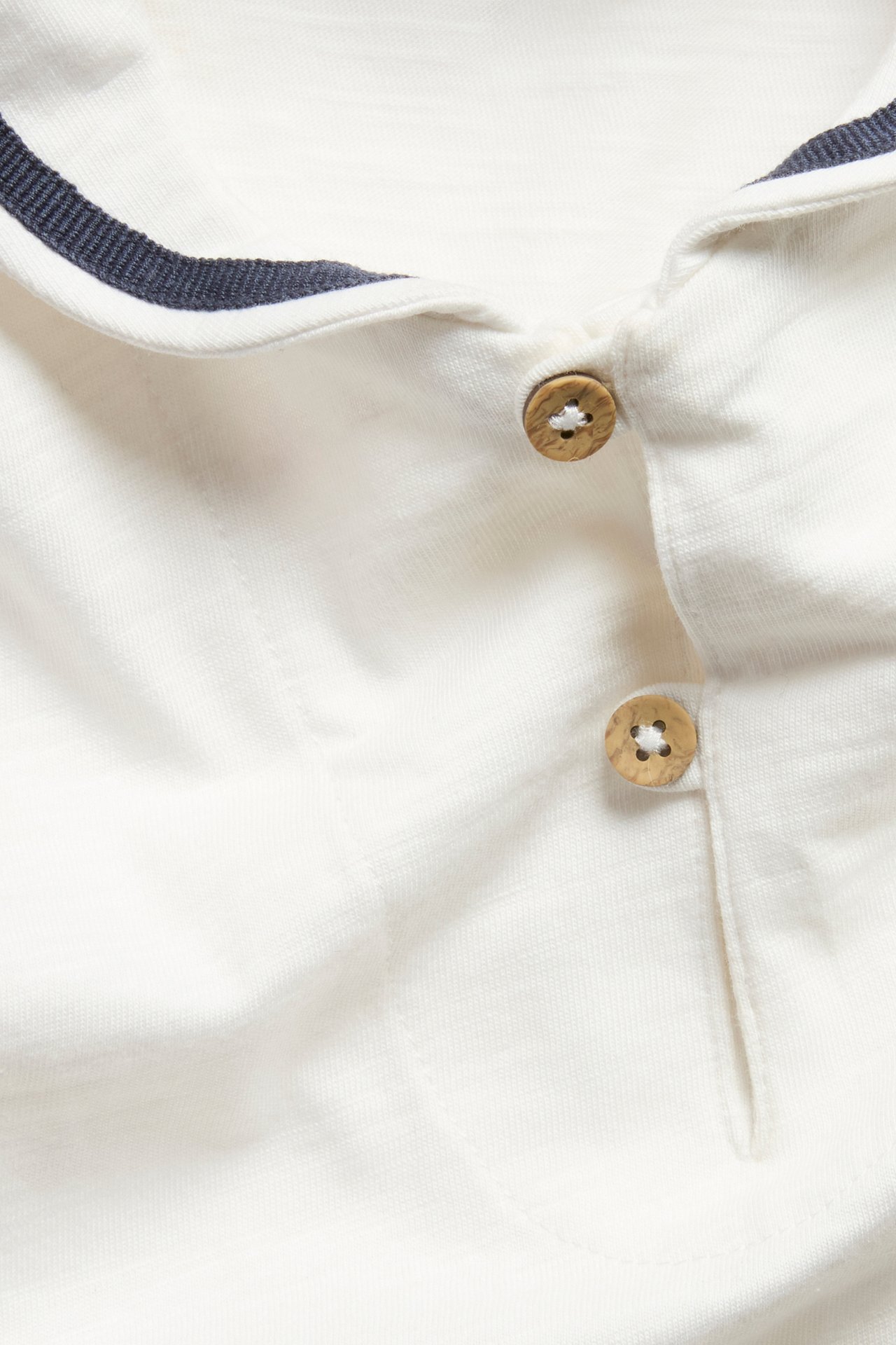 Nahaufnahme eines cremeweißen Baby-Kurzarmbodys mit maritimem Kragen mit dunkelblauem Streifen und Holzknöpfen.
