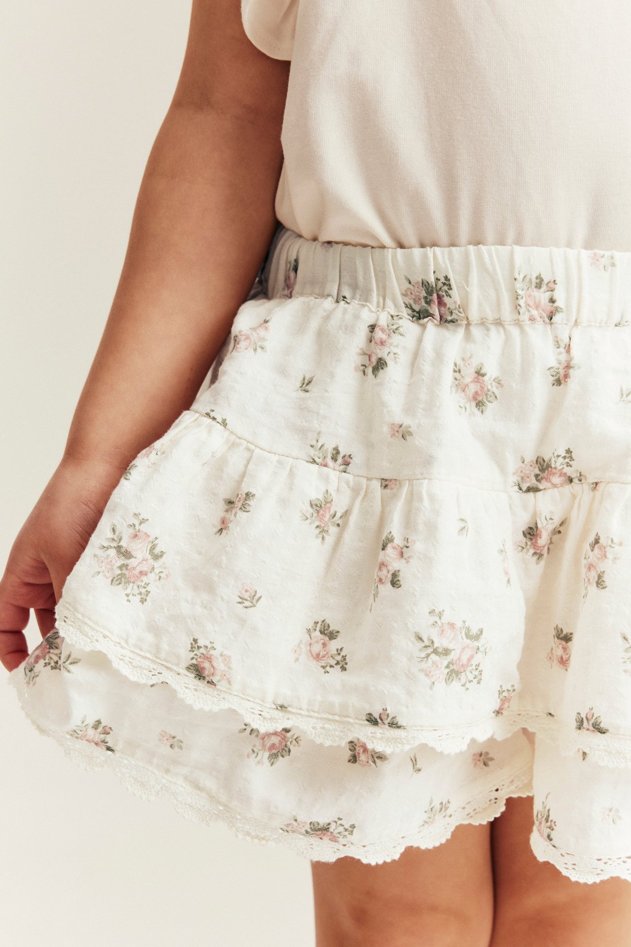 Close-up of kid wearing an off-white floral cotton shorts-skirt with ruffles and lace trim.